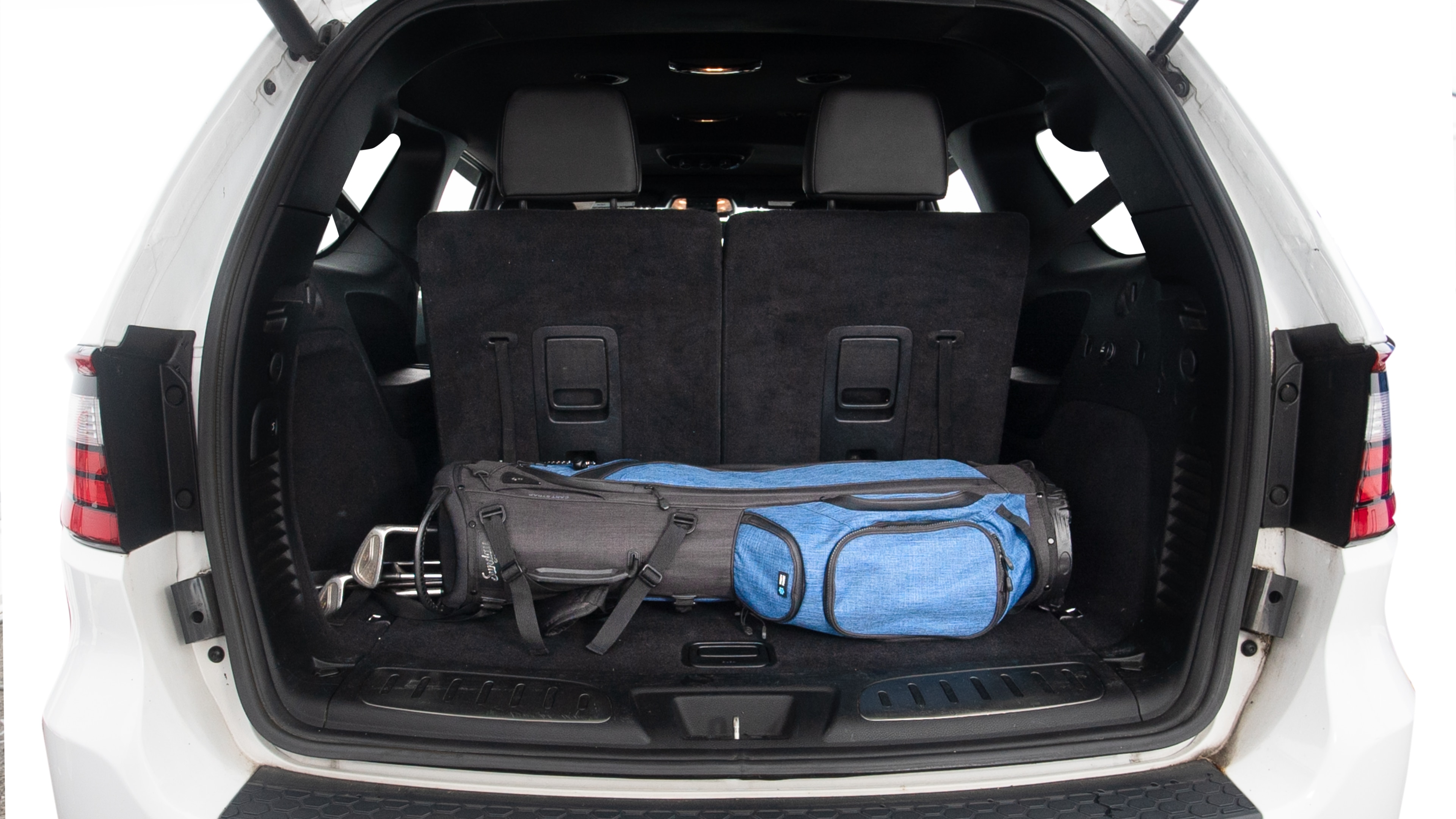 The trunk lid is open showing full view of the trunk. Three grocery carriers, two camping chairs in the carrying bag, and a set of golf clubs are placed inside.