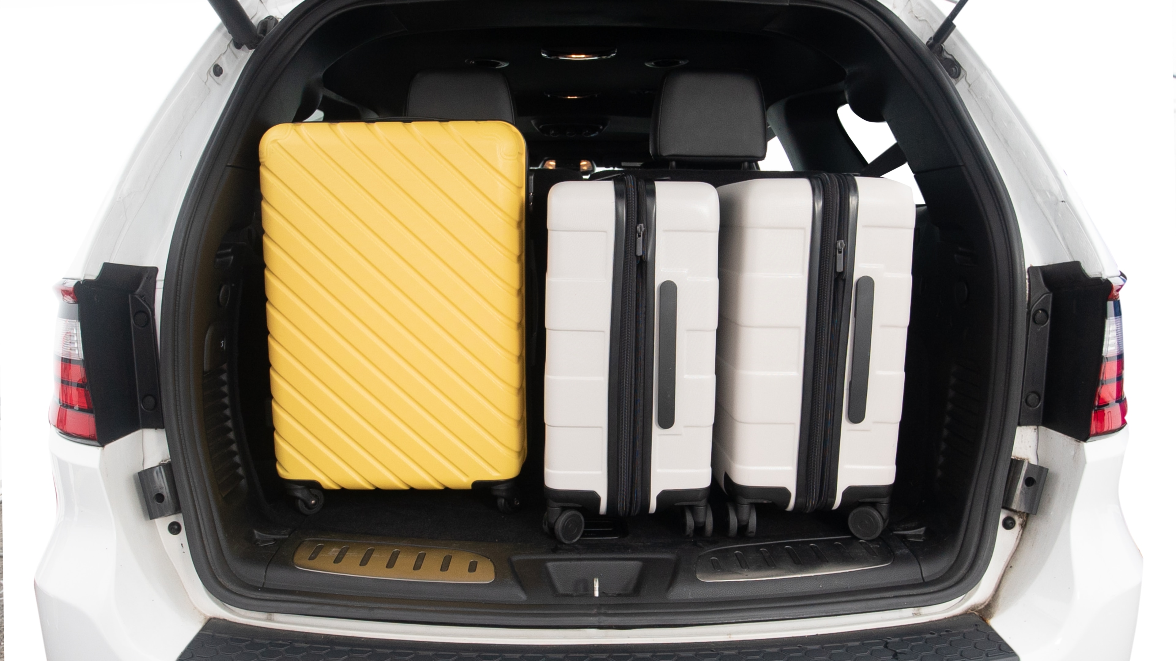 The trunk lid is open, showing full view of the trunk space. One large and two small suitcases are placed inside.