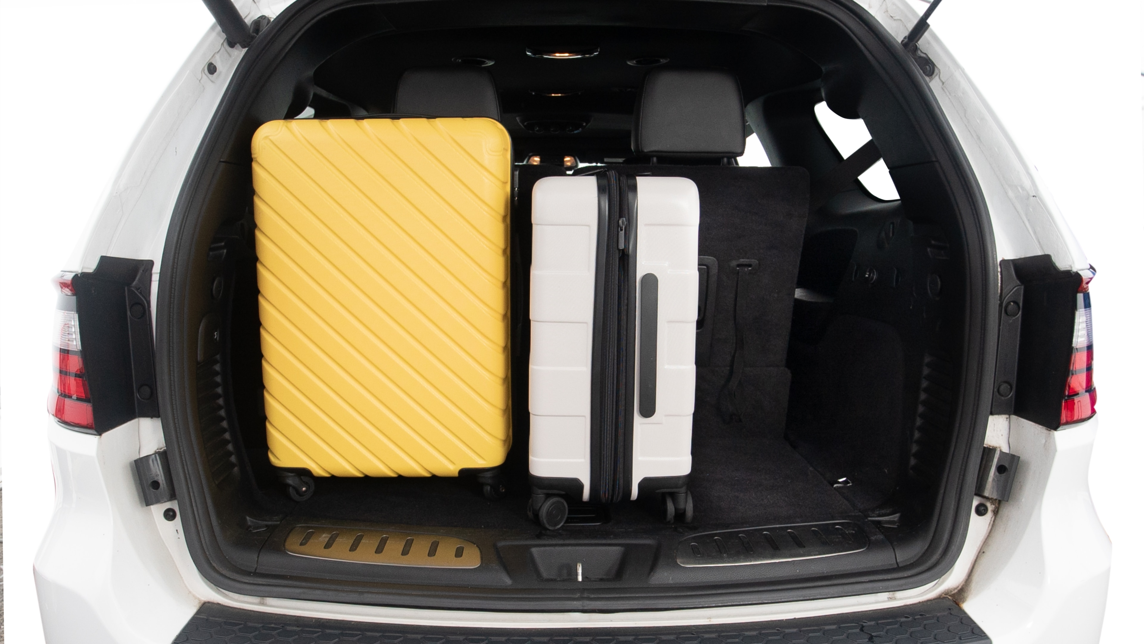 The trunk lid is open, showing full view of the trunk space. One large and two small suitcases are placed inside.