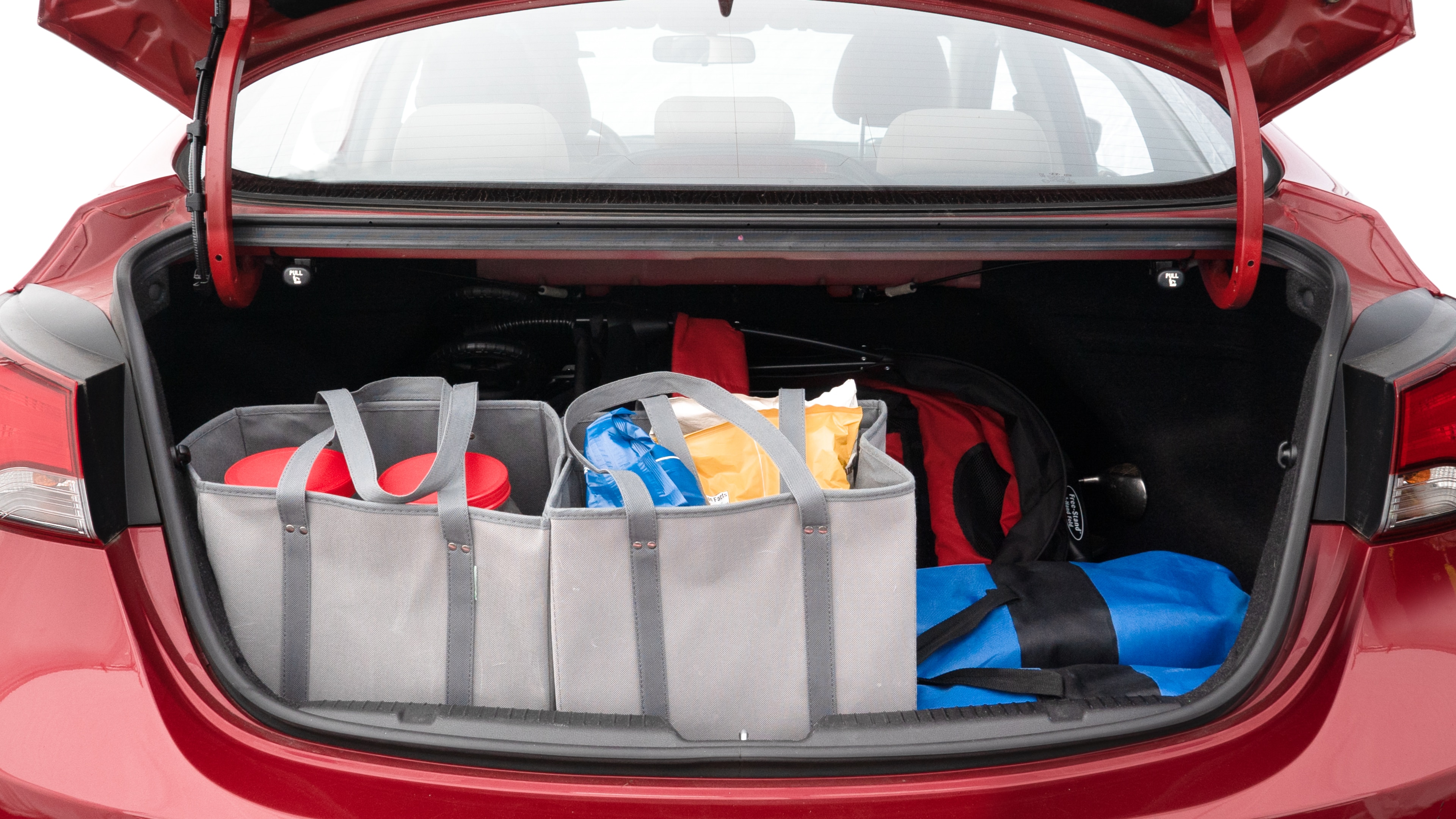 The trunk lid is open showing full view of the trunk. A baby stroller, three grocery carriers, two camping chairs in the carrying bag, and a set of golf clubs are placed inside.