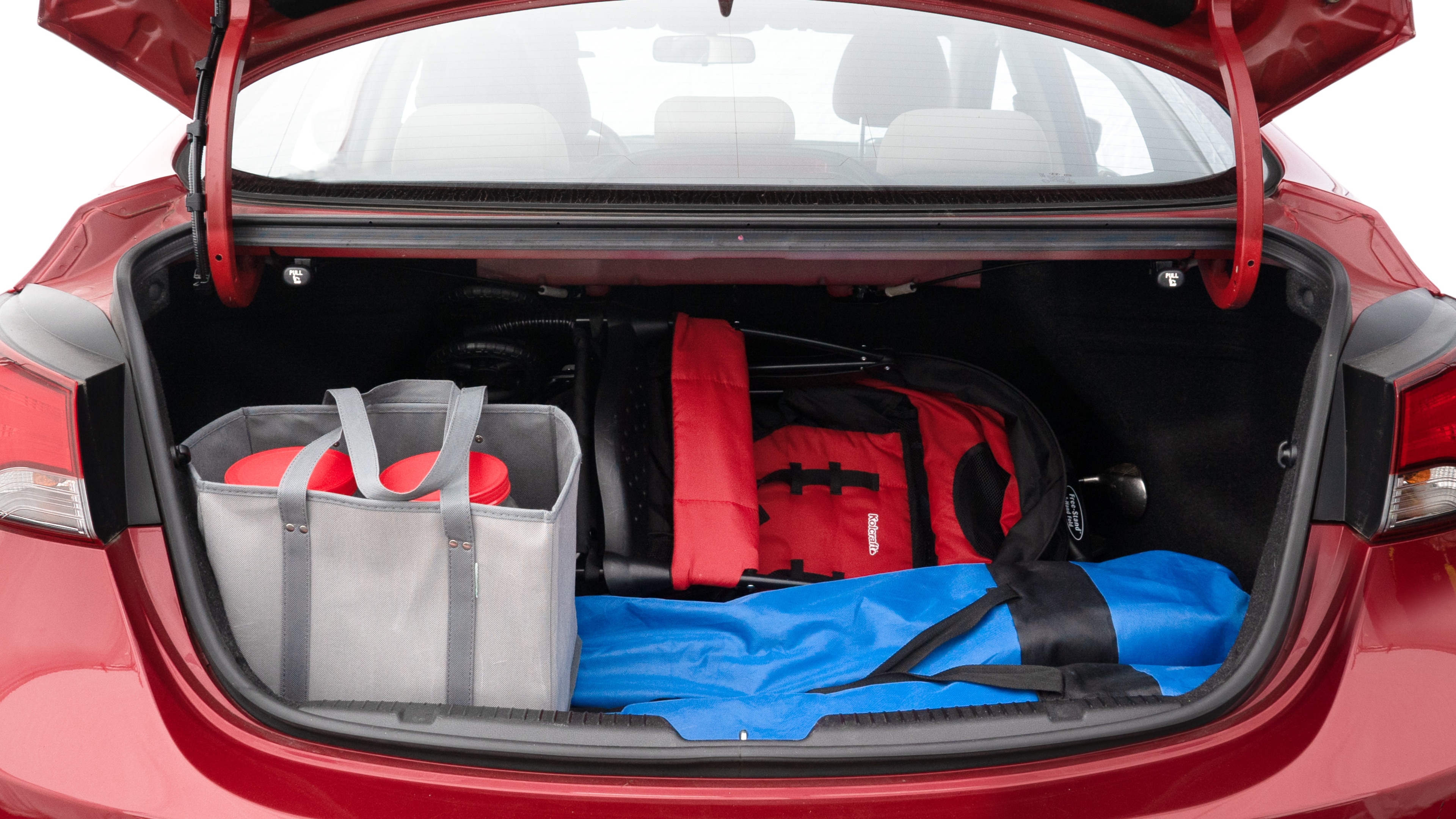 The trunk lid is open showing full view of the trunk. A baby stroller, three grocery carriers, two camping chairs in the carrying bag, and a set of golf clubs are placed inside.