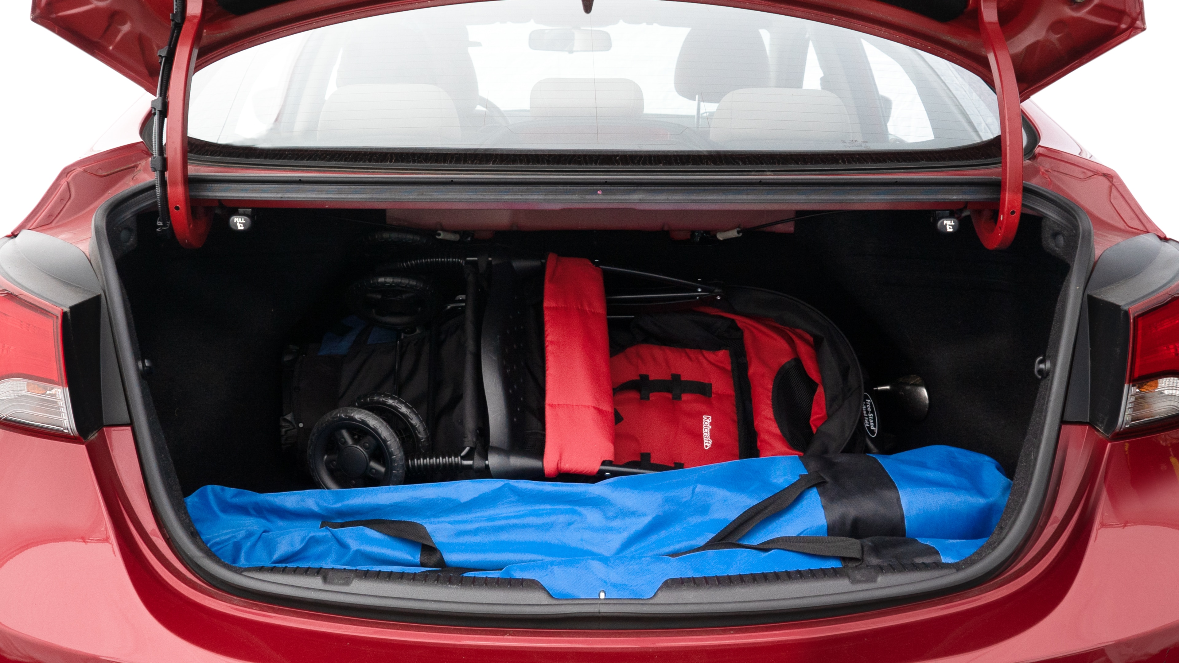 The trunk lid is open showing full view of the trunk. A baby stroller, three grocery carriers, two camping chairs in the carrying bag, and a set of golf clubs are placed inside.