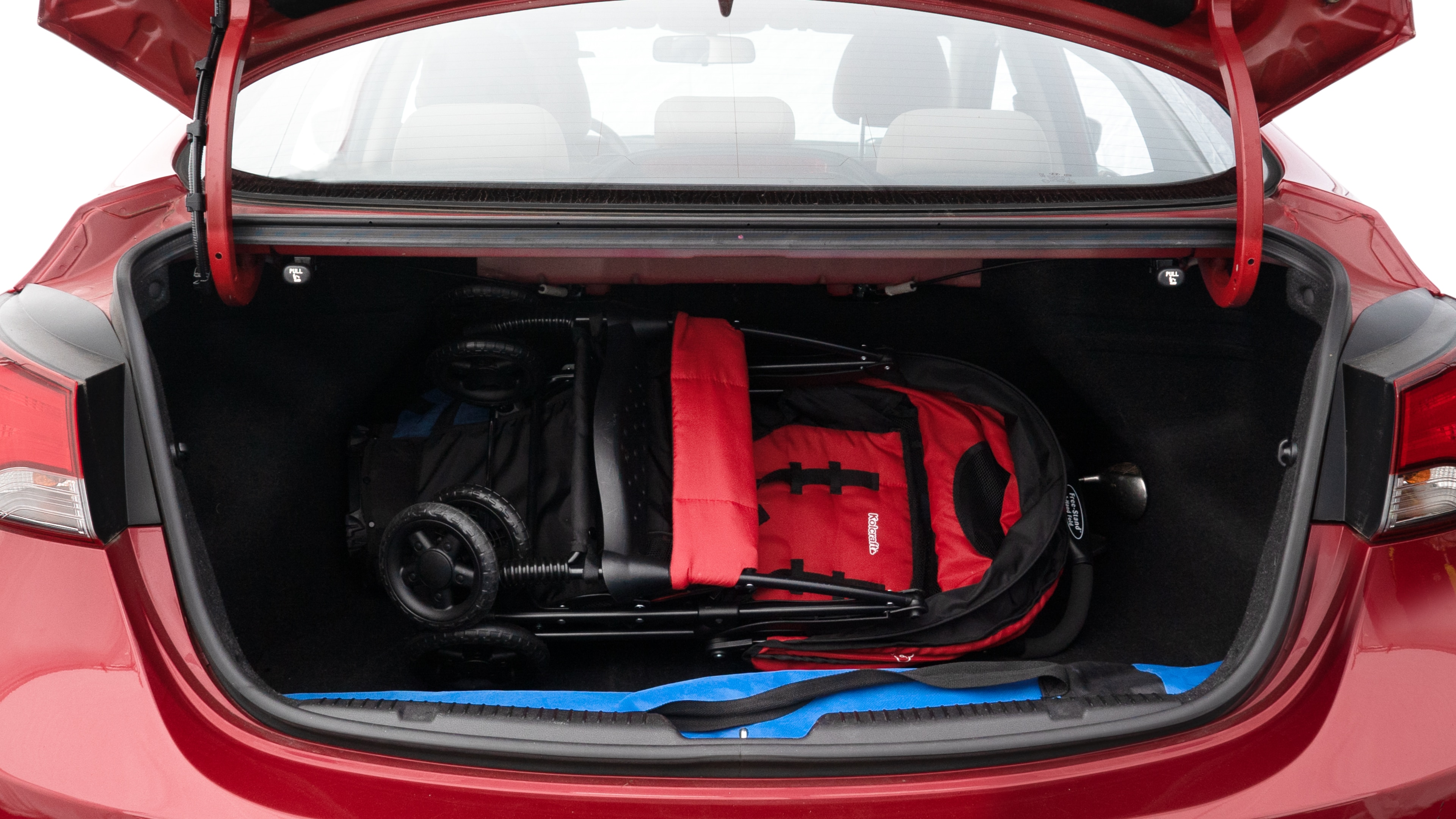 The trunk lid is open showing full view of the trunk. A baby stroller, three grocery carriers, two camping chairs in the carrying bag, and a set of golf clubs are placed inside.
