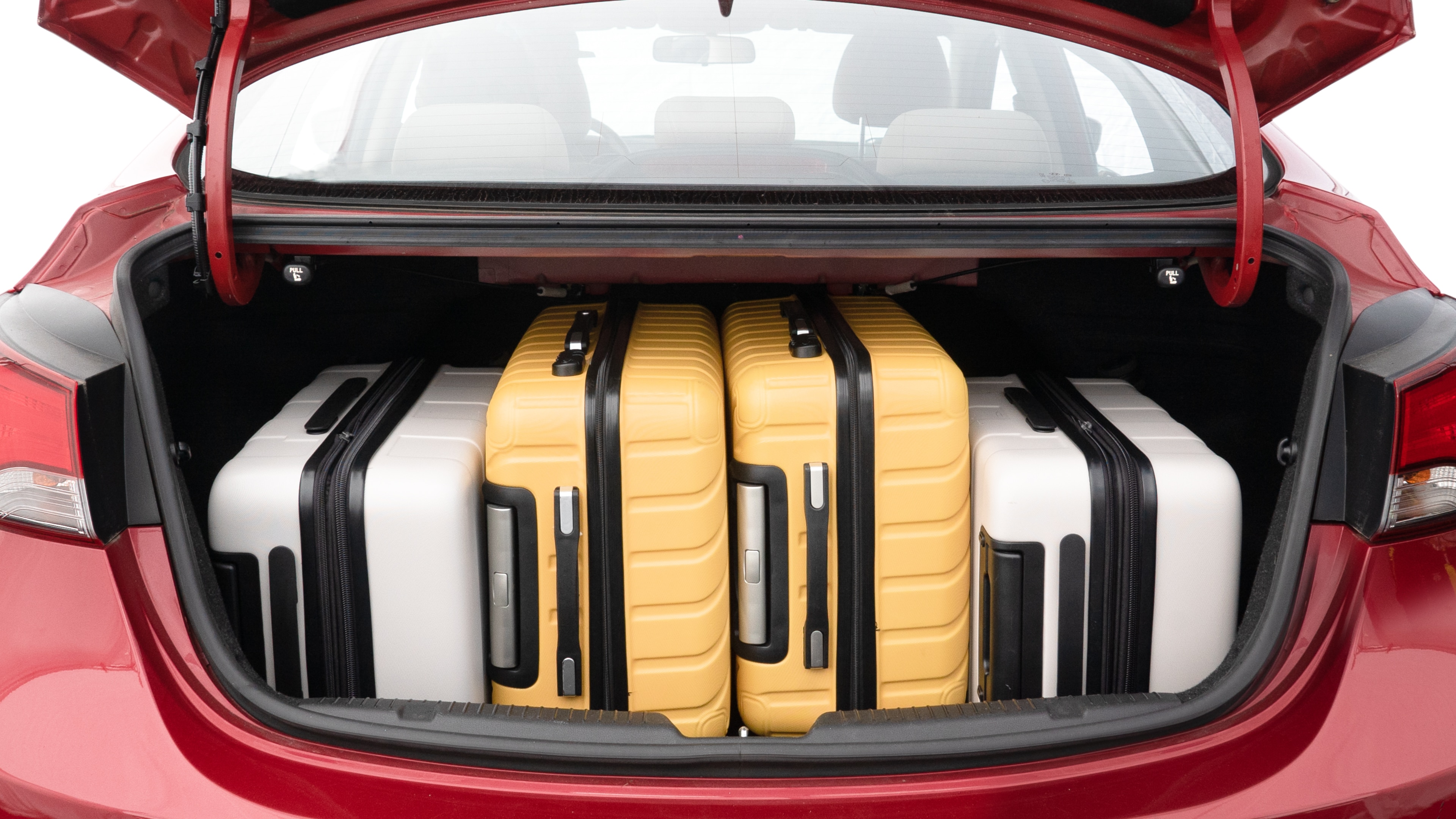 The trunk lid is open, showing full view of the trunk space. Two medium and two small suitcases are placed inside.