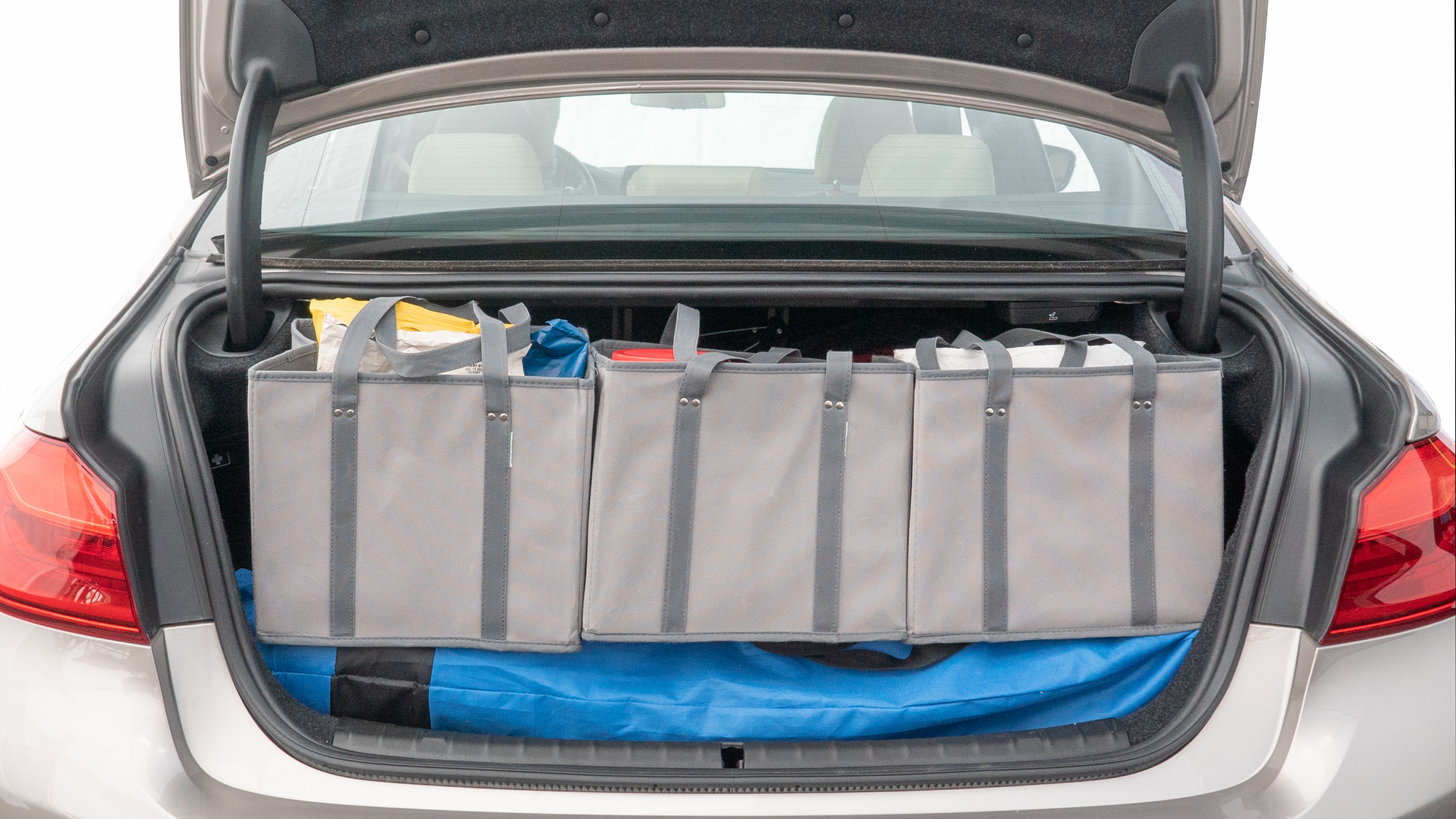 The trunk lid is open showing full view of the trunk. A baby stroller, three grocery carriers, two camping chairs in the carrying bag, and a set of golf clubs are placed inside.