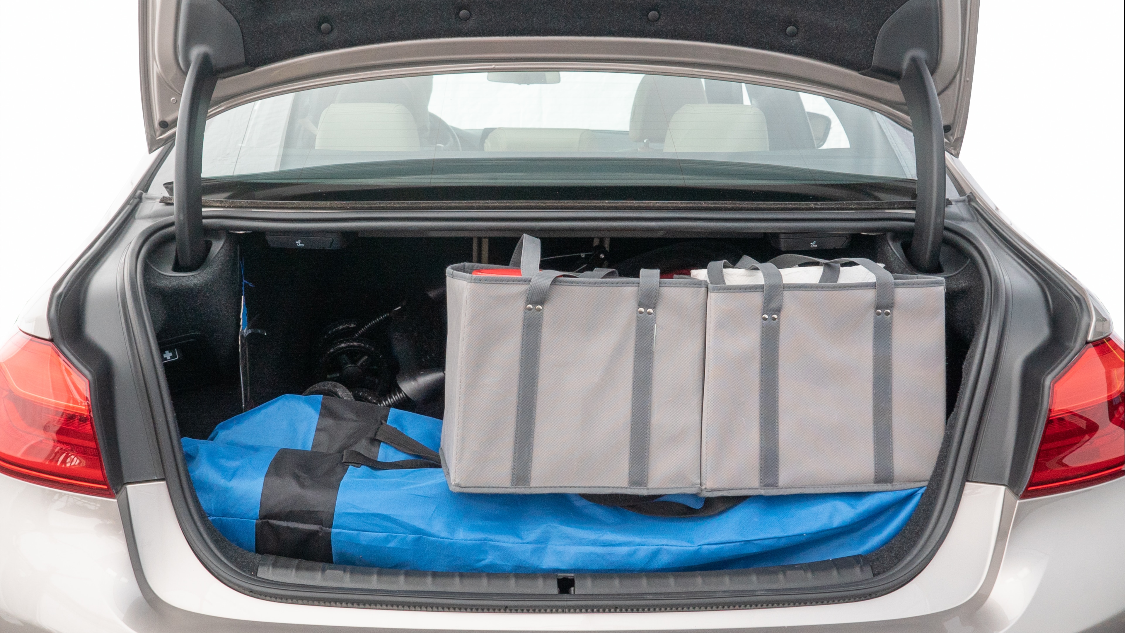 The trunk lid is open showing full view of the trunk. A baby stroller, three grocery carriers, two camping chairs in the carrying bag, and a set of golf clubs are placed inside.