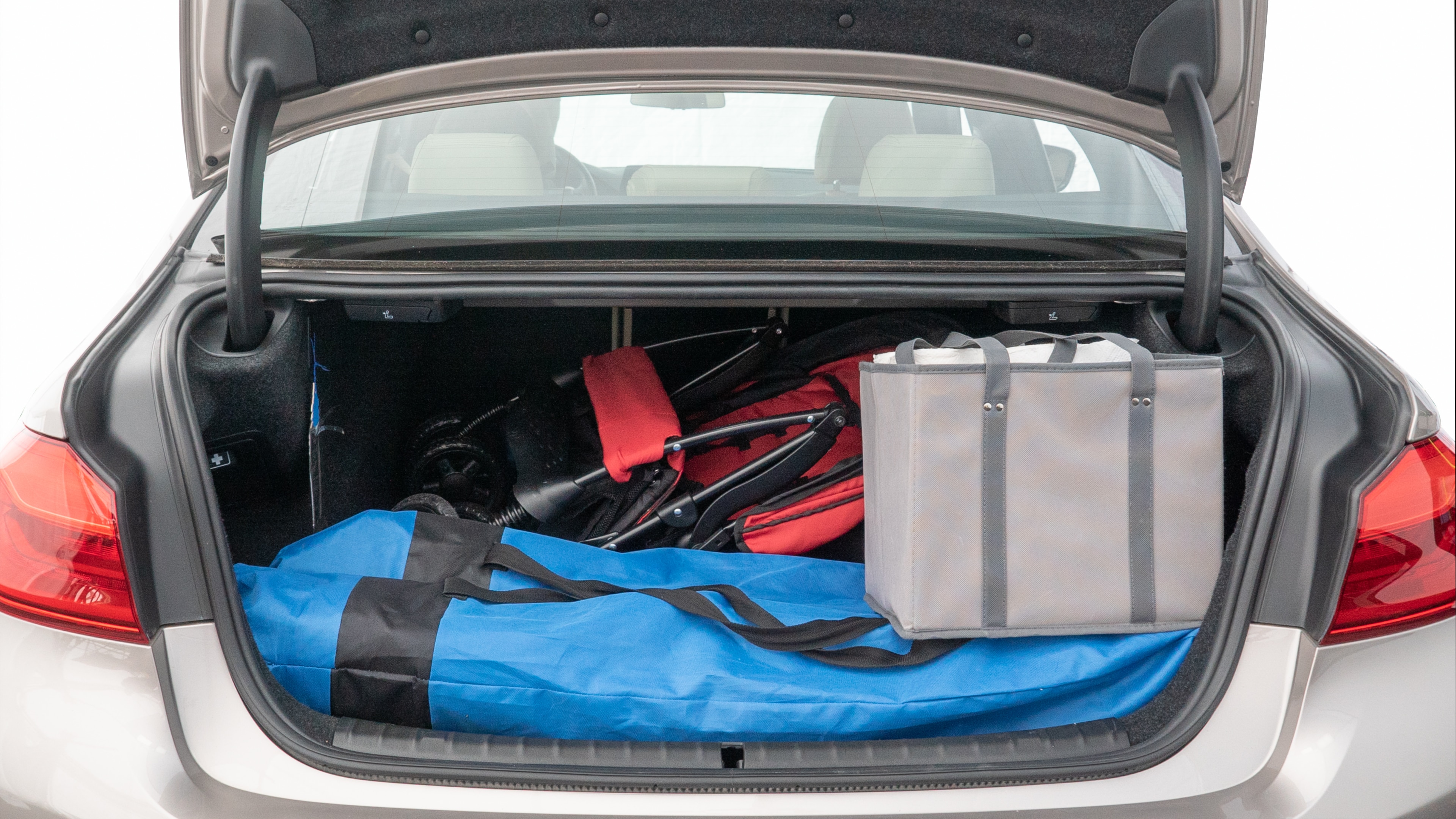 The trunk lid is open showing full view of the trunk. A baby stroller, three grocery carriers, two camping chairs in the carrying bag, and a set of golf clubs are placed inside.