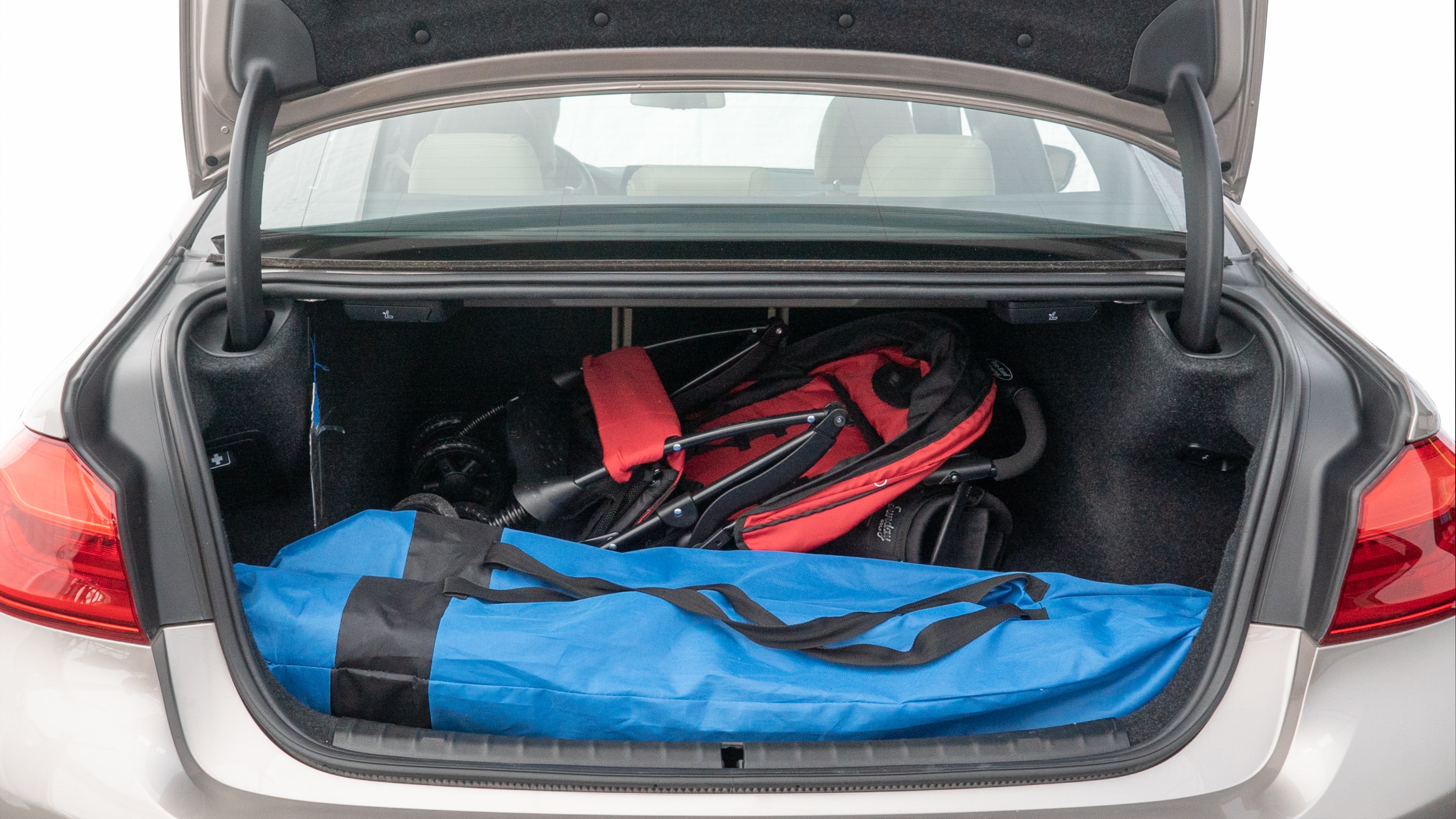 The trunk lid is open showing full view of the trunk. A baby stroller, three grocery carriers, two camping chairs in the carrying bag, and a set of golf clubs are placed inside.