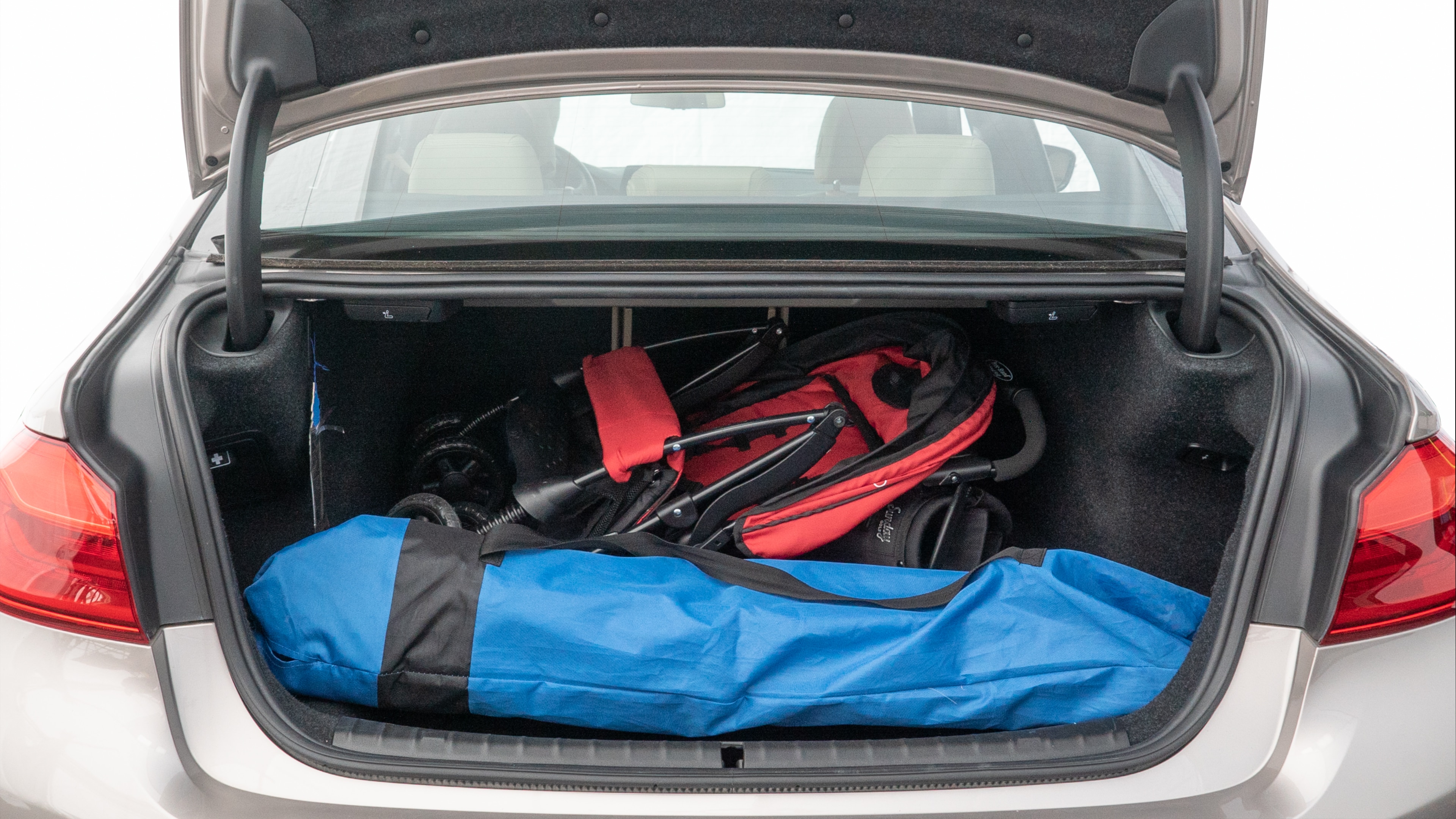 The trunk lid is open showing full view of the trunk. A baby stroller, three grocery carriers, two camping chairs in the carrying bag, and a set of golf clubs are placed inside.