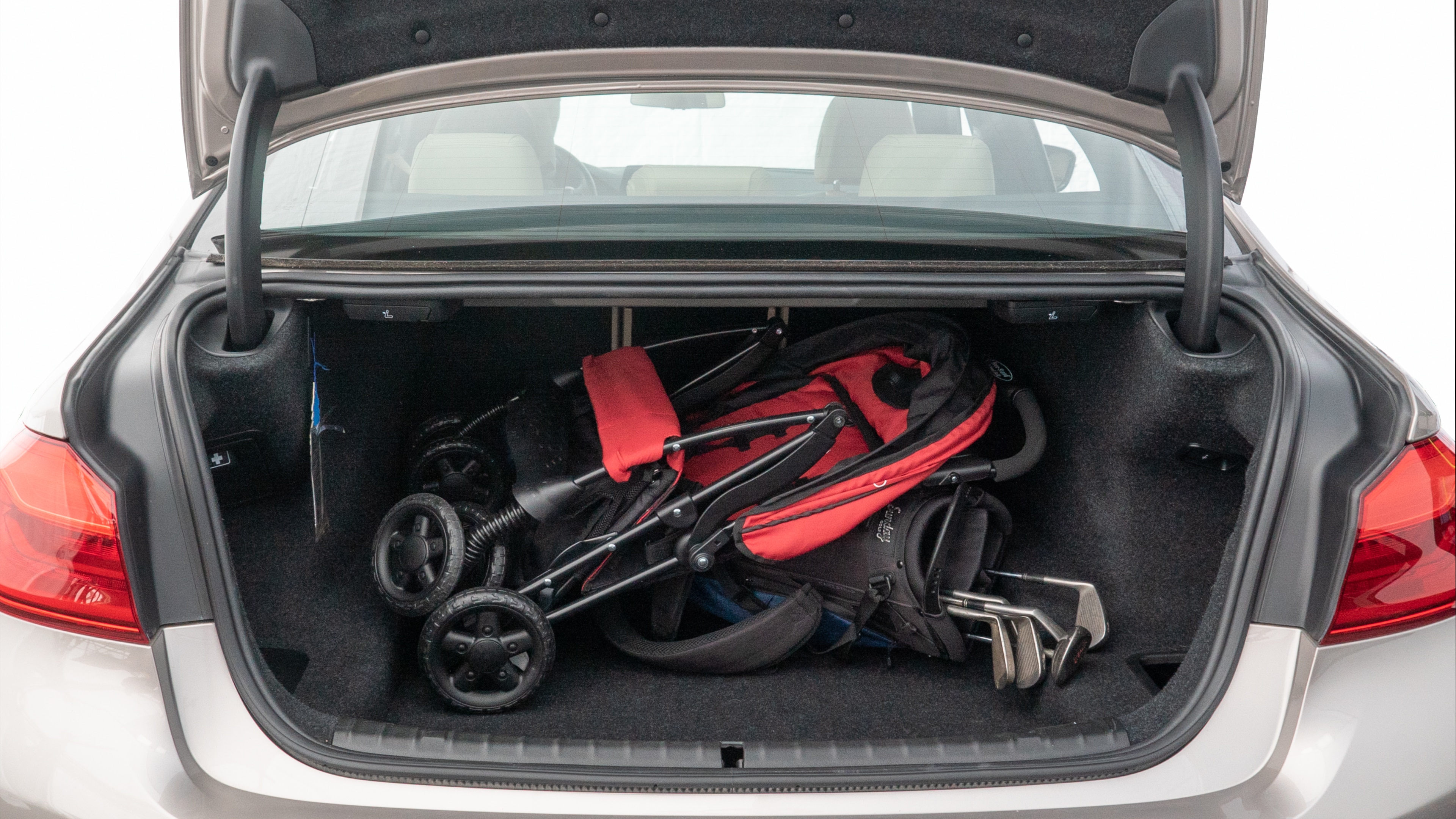 The trunk lid is open showing full view of the trunk. A baby stroller, three grocery carriers, two camping chairs in the carrying bag, and a set of golf clubs are placed inside.