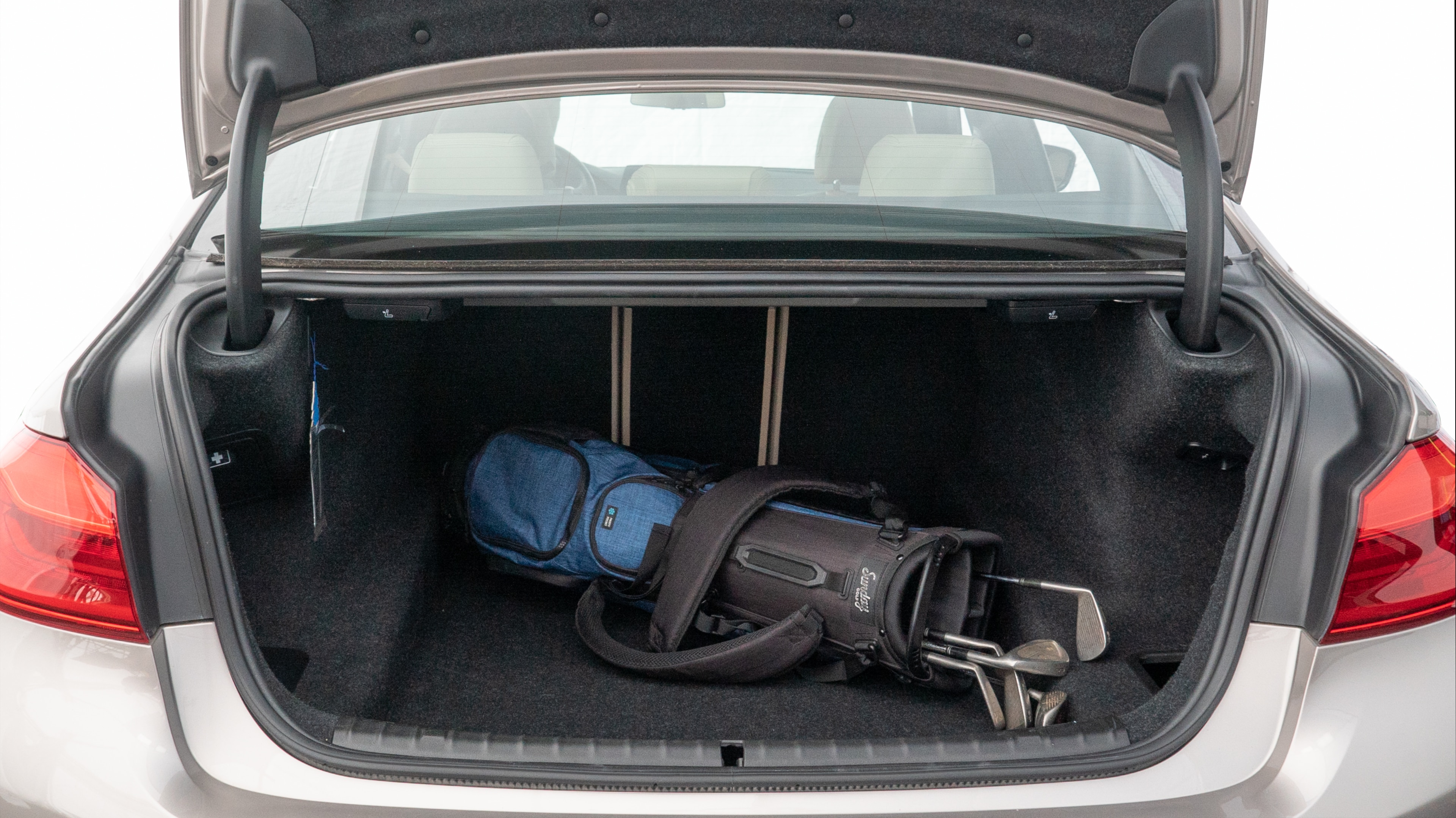 The trunk lid is open showing full view of the trunk. A baby stroller, three grocery carriers, two camping chairs in the carrying bag, and a set of golf clubs are placed inside.