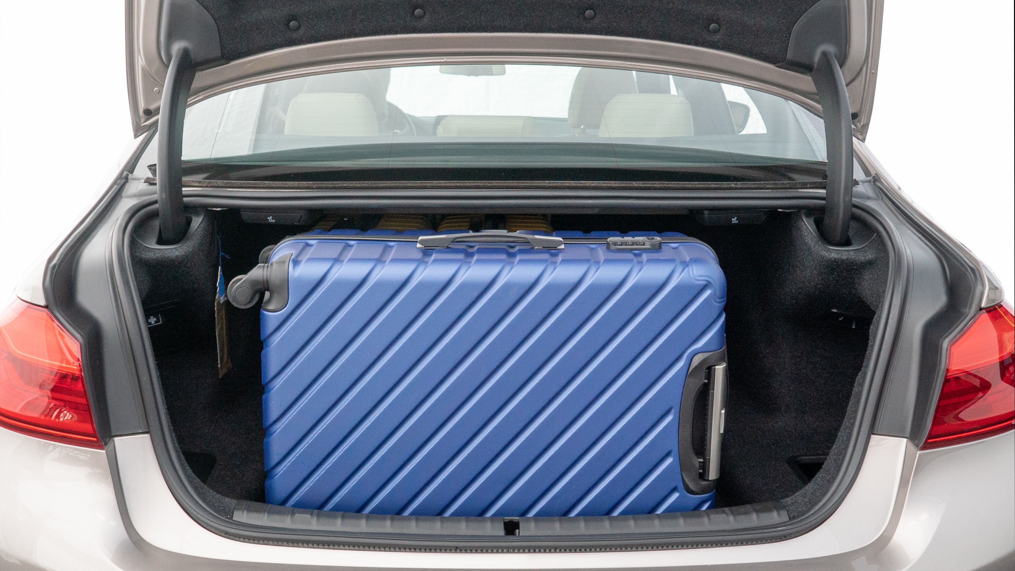 The trunk lid is open, showing full view of the trunk space. Two medium and two small suitcases are placed inside.