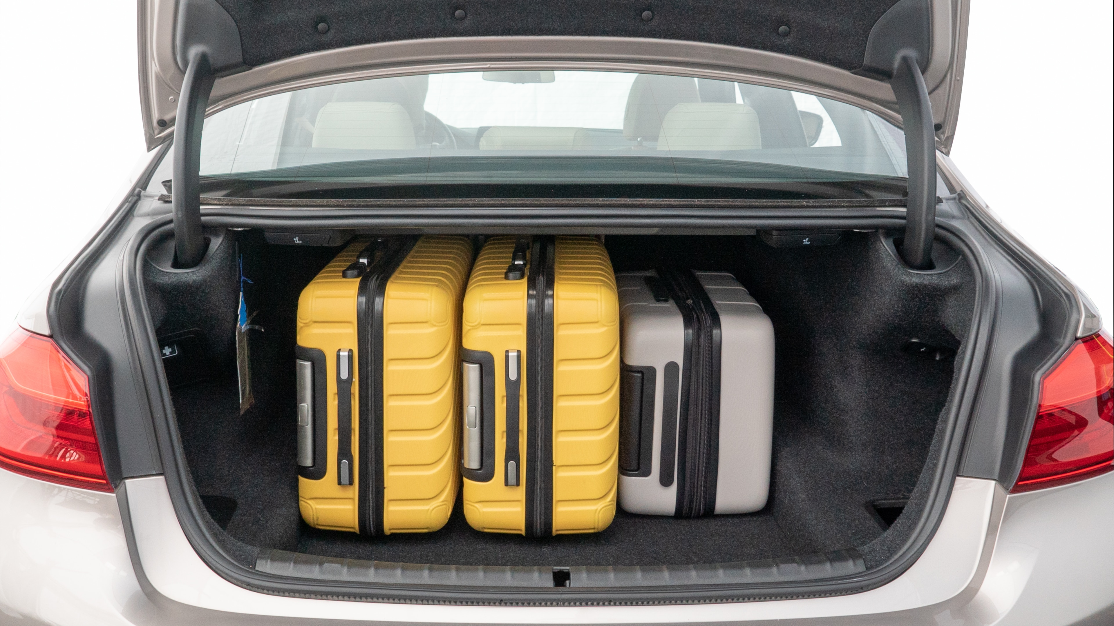 The trunk lid is open, showing full view of the trunk space. Two medium and two small suitcases are placed inside.