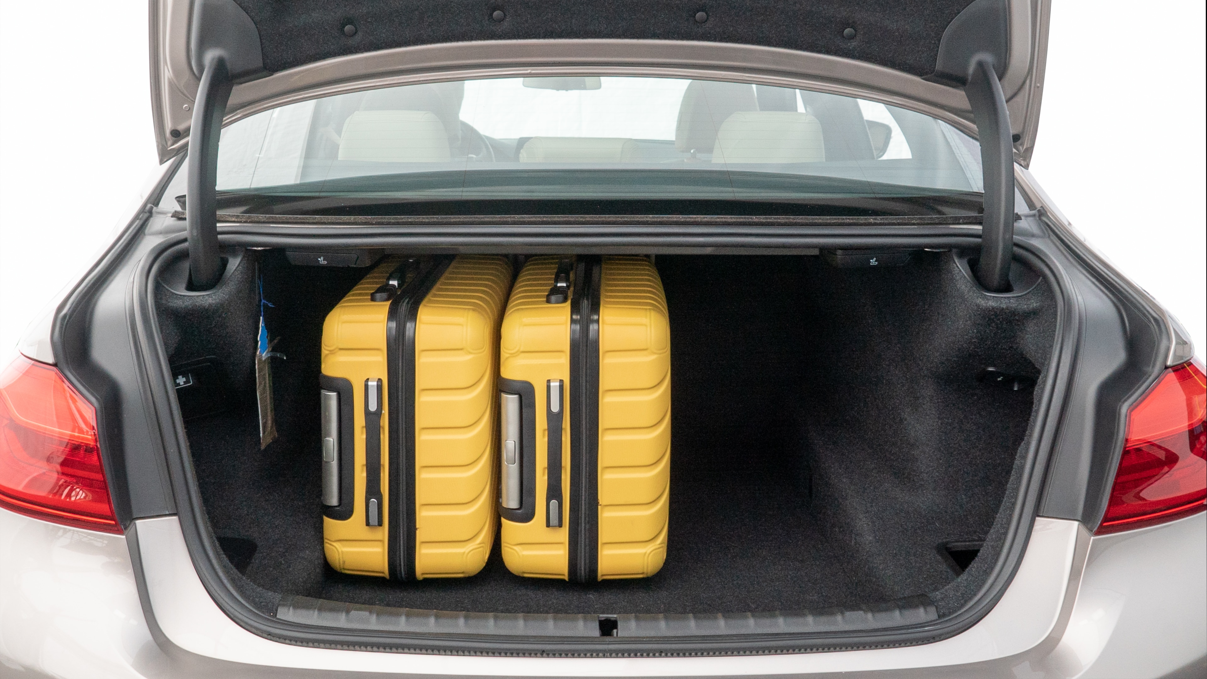 The trunk lid is open, showing full view of the trunk space. Two medium and two small suitcases are placed inside.