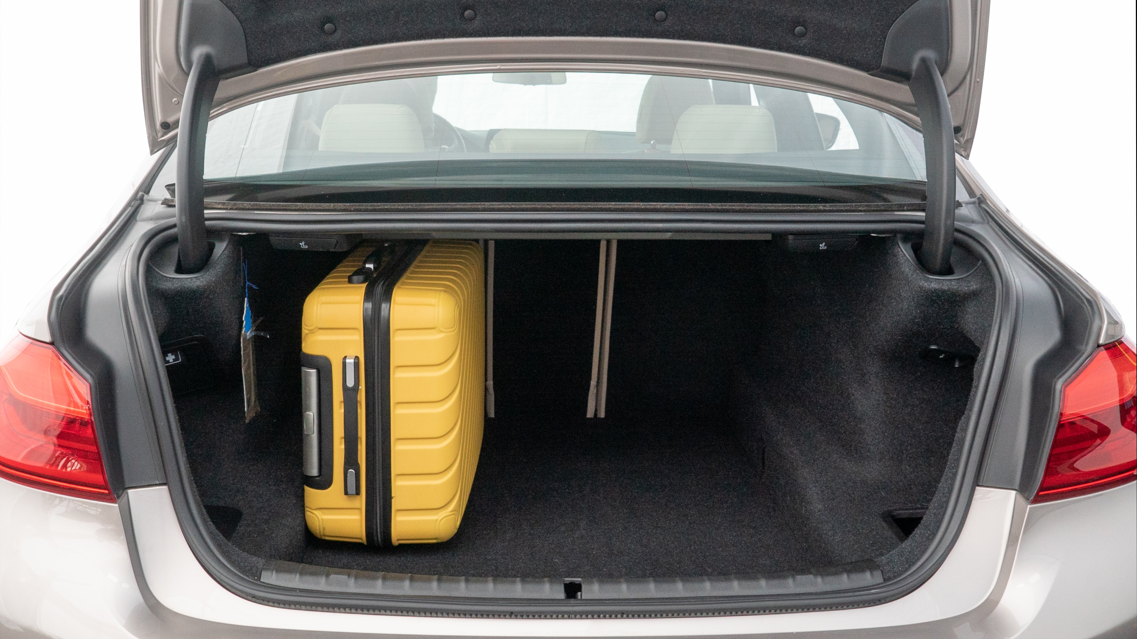The trunk lid is open, showing full view of the trunk space. Two medium and two small suitcases are placed inside.