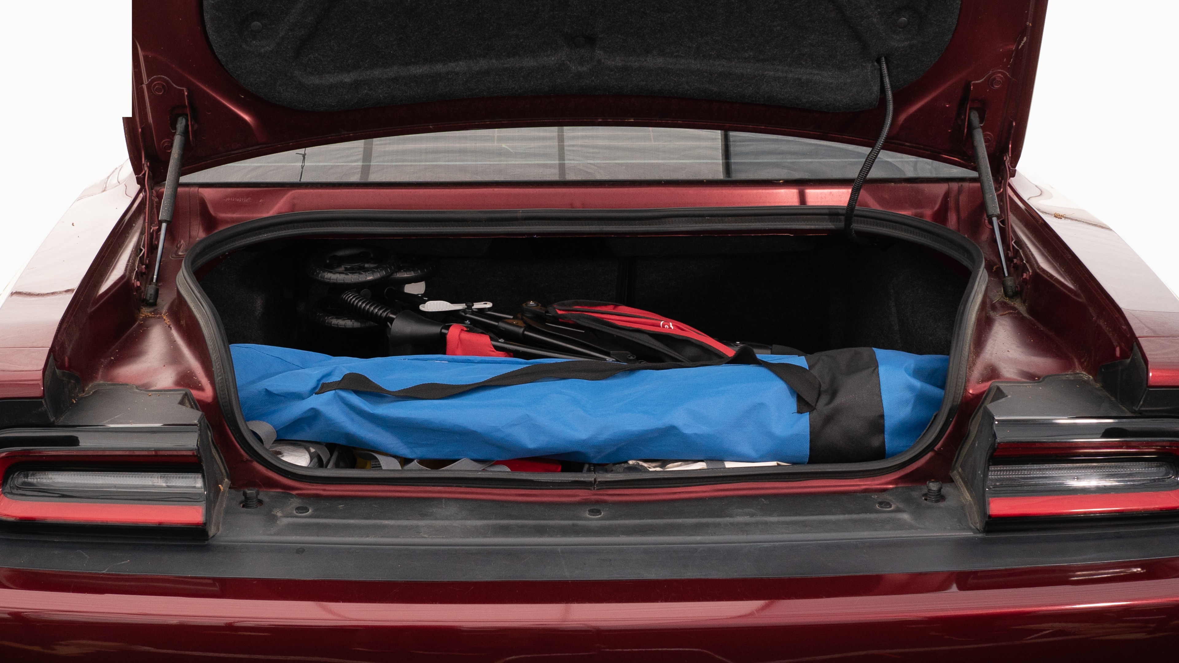 The trunk lid is open showing full view of the trunk. A baby stroller, four grocery carriers, a yoga mat, and a set of golf clubs are placed inside