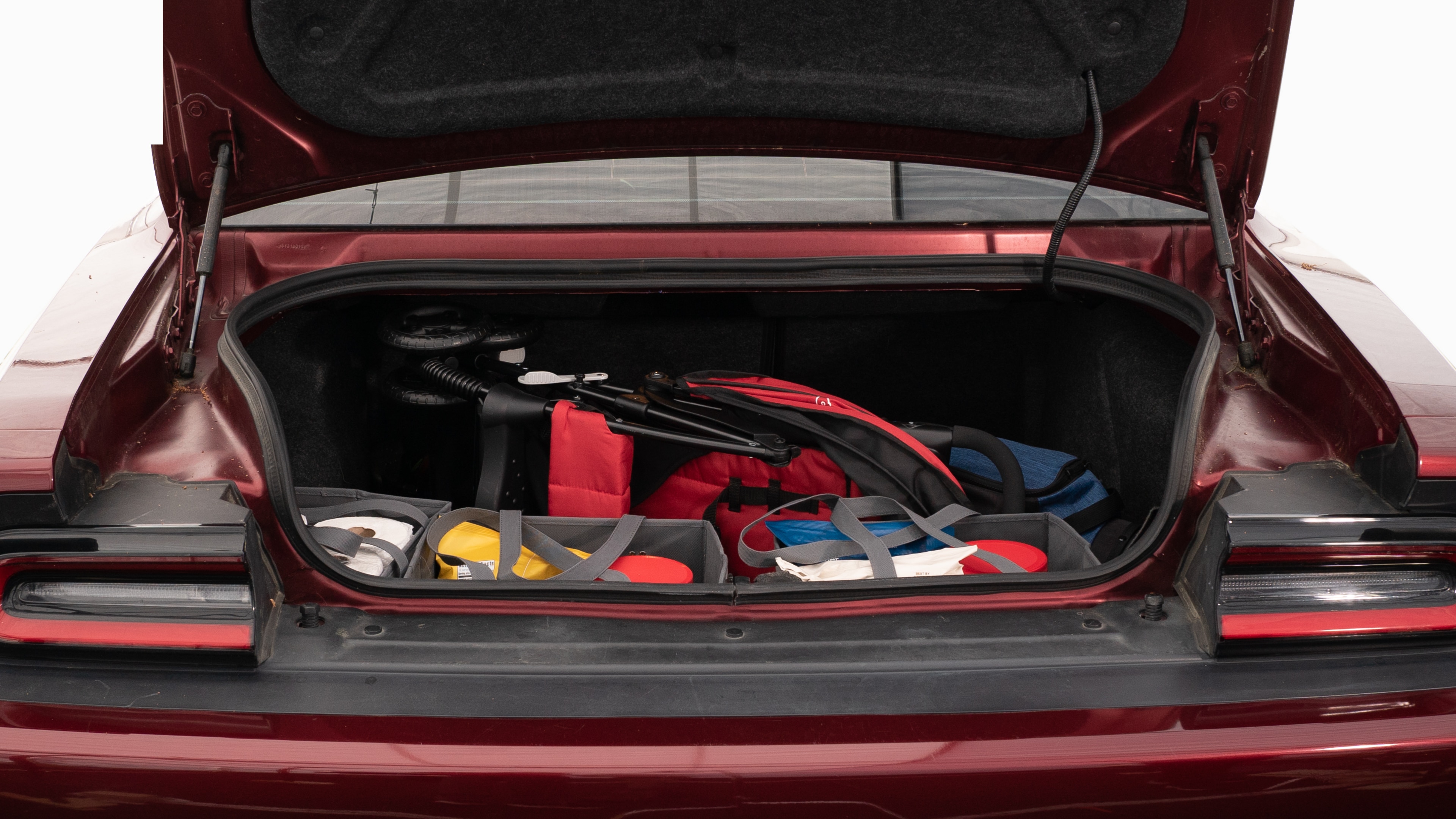 The trunk lid is open showing full view of the trunk. A baby stroller, four grocery carriers, a yoga mat, and a set of golf clubs are placed inside