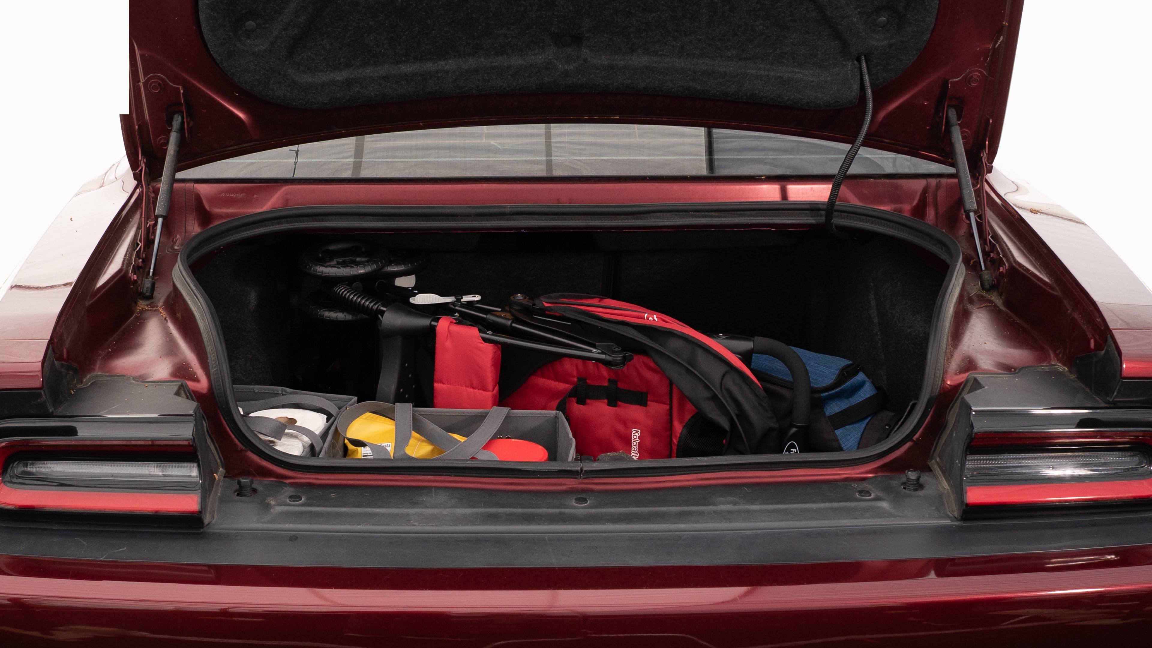 The trunk lid is open showing full view of the trunk. A baby stroller, four grocery carriers, a yoga mat, and a set of golf clubs are placed inside