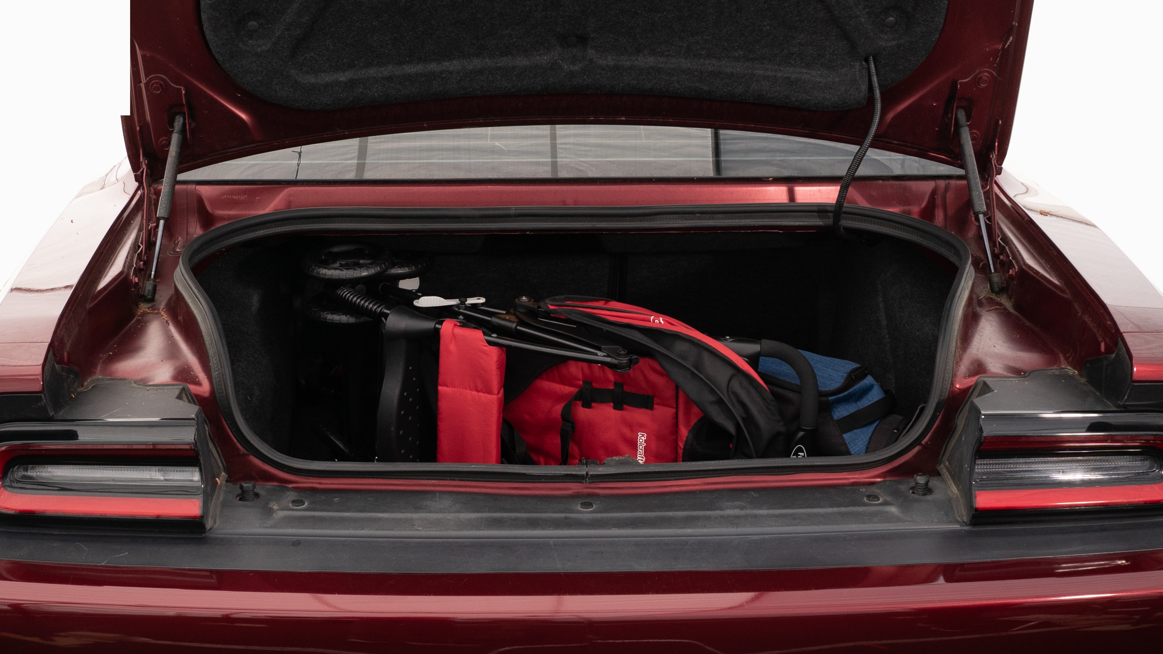 The trunk lid is open showing full view of the trunk. A baby stroller, four grocery carriers, a yoga mat, and a set of golf clubs are placed inside