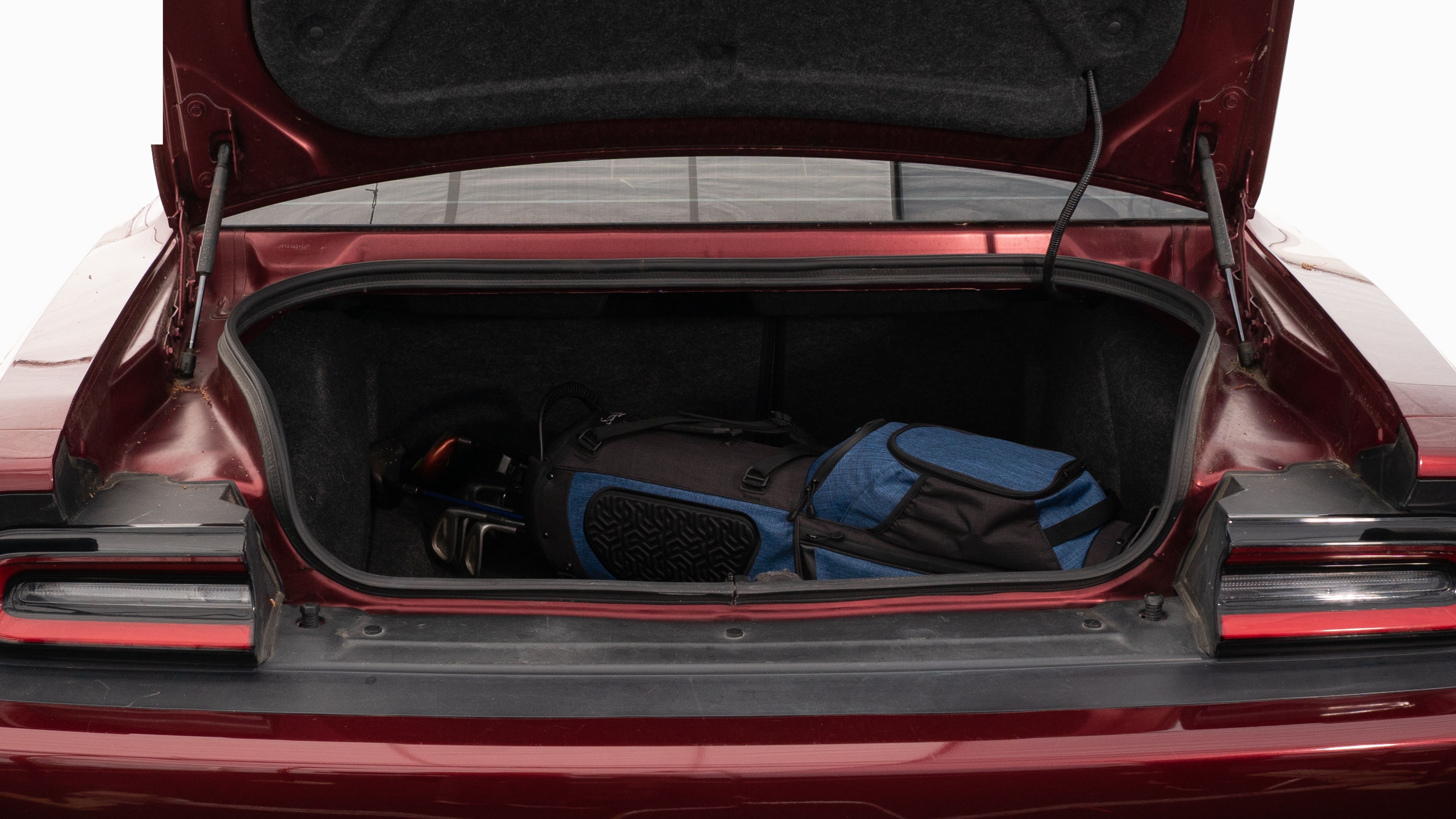 The trunk lid is open showing full view of the trunk. A baby stroller, four grocery carriers, a yoga mat, and a set of golf clubs are placed inside