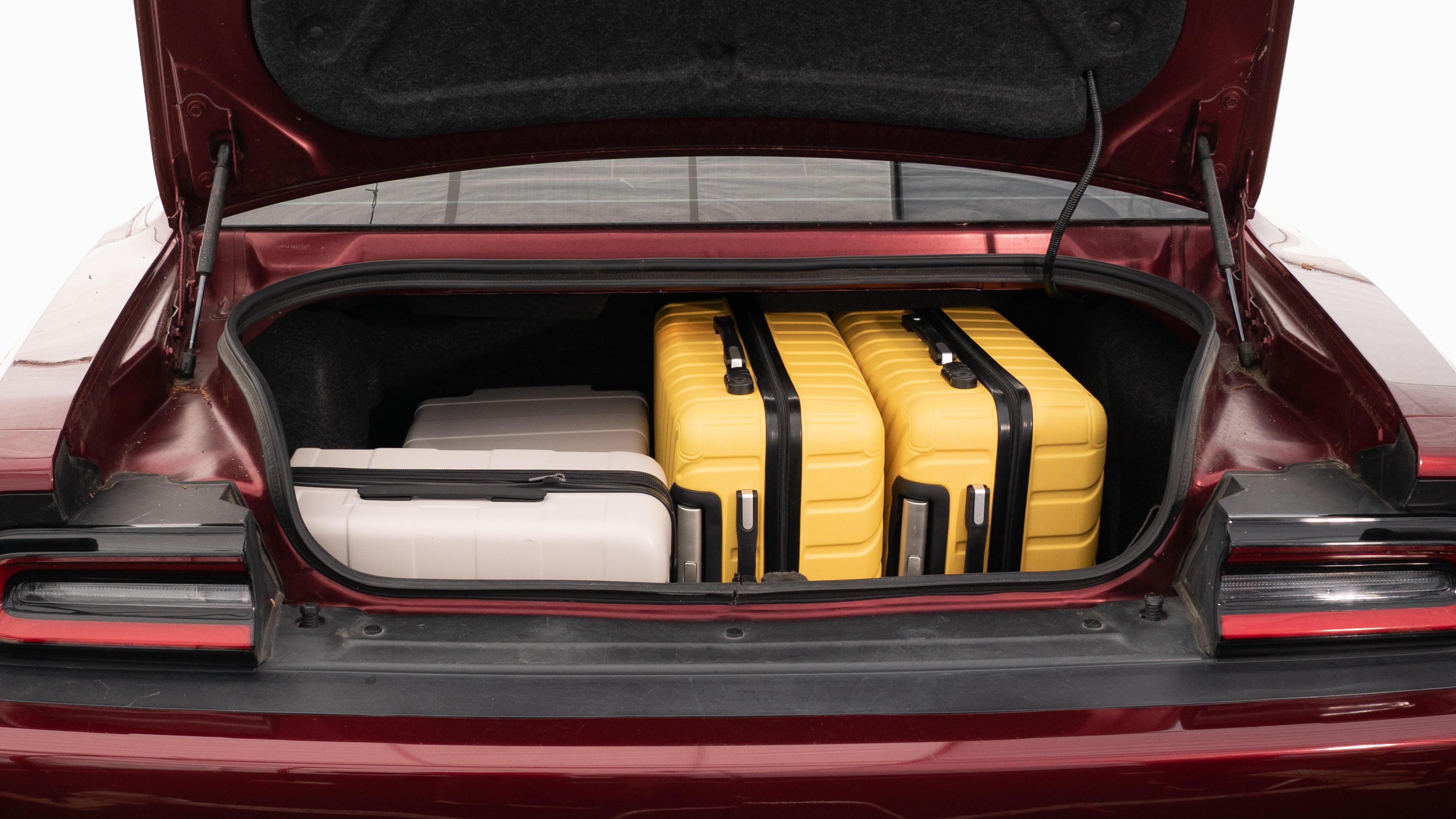 The trunk lid is open, showing full view of the trunk space. Two large and two small suitcases are placed on their sides.