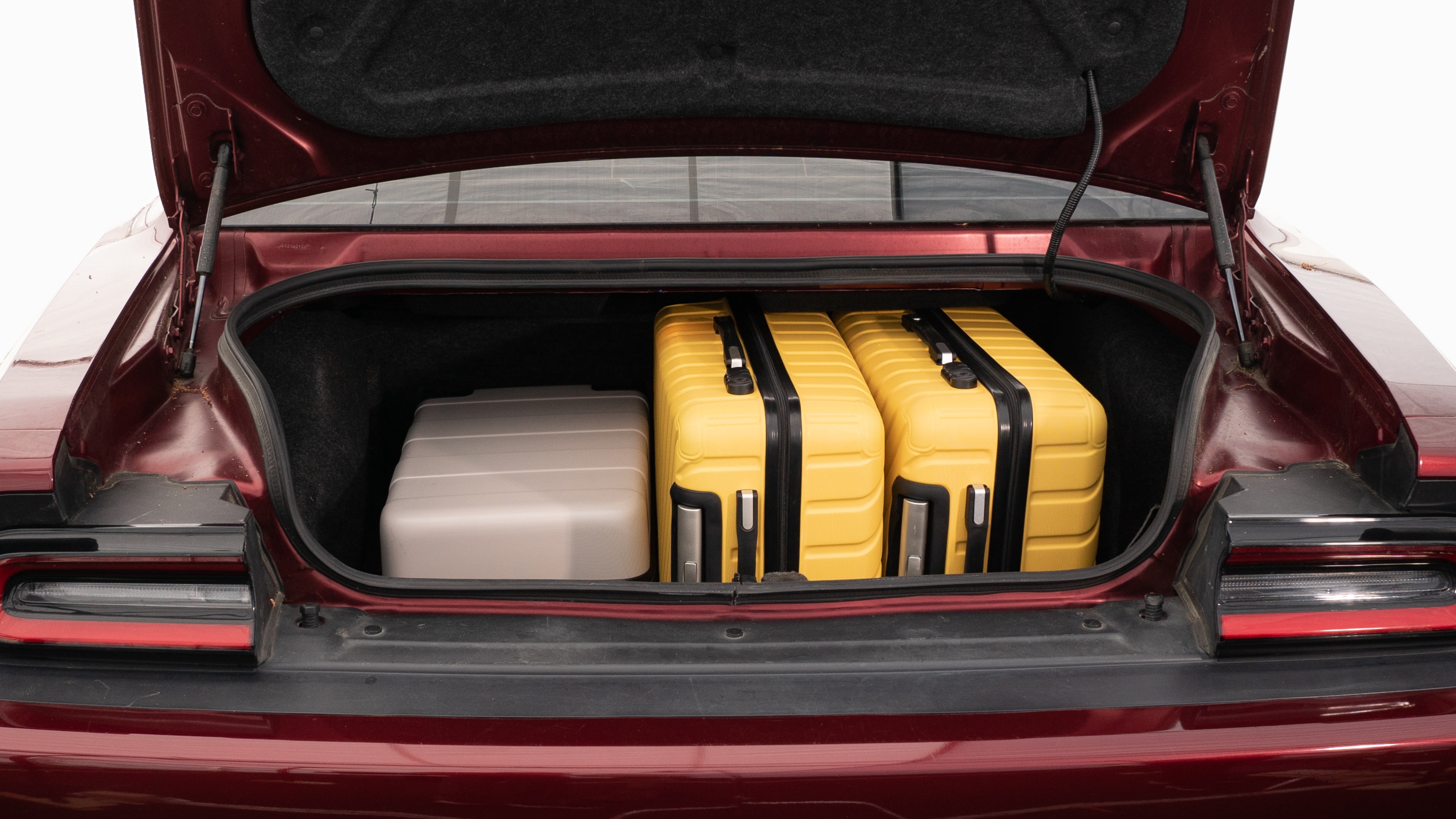 The trunk lid is open, showing full view of the trunk space. Two large and two small suitcases are placed on their sides.