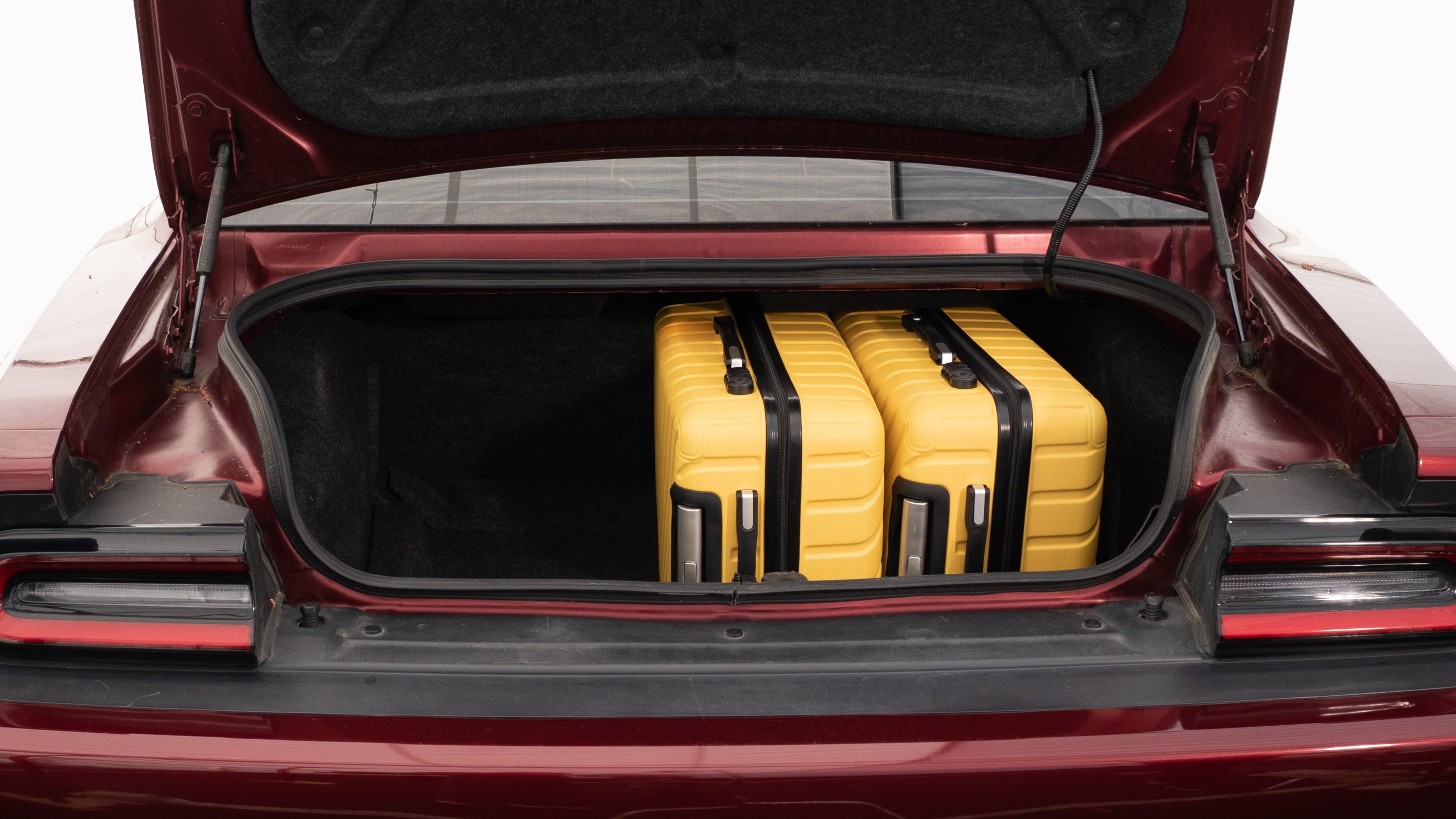 The trunk lid is open, showing full view of the trunk space. Two large and two small suitcases are placed on their sides.
