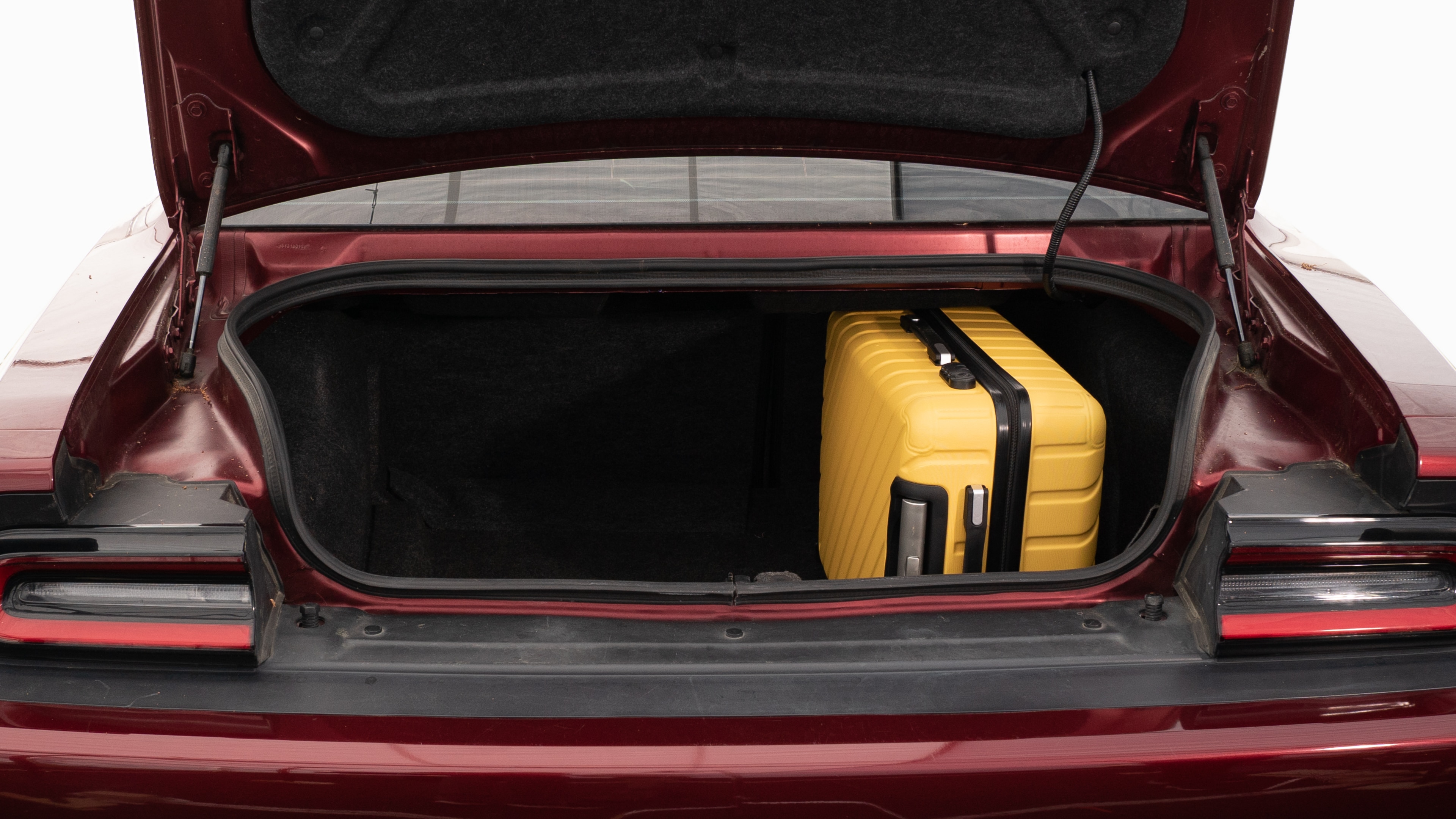 The trunk lid is open, showing full view of the trunk space. Two large and two small suitcases are placed on their sides.
