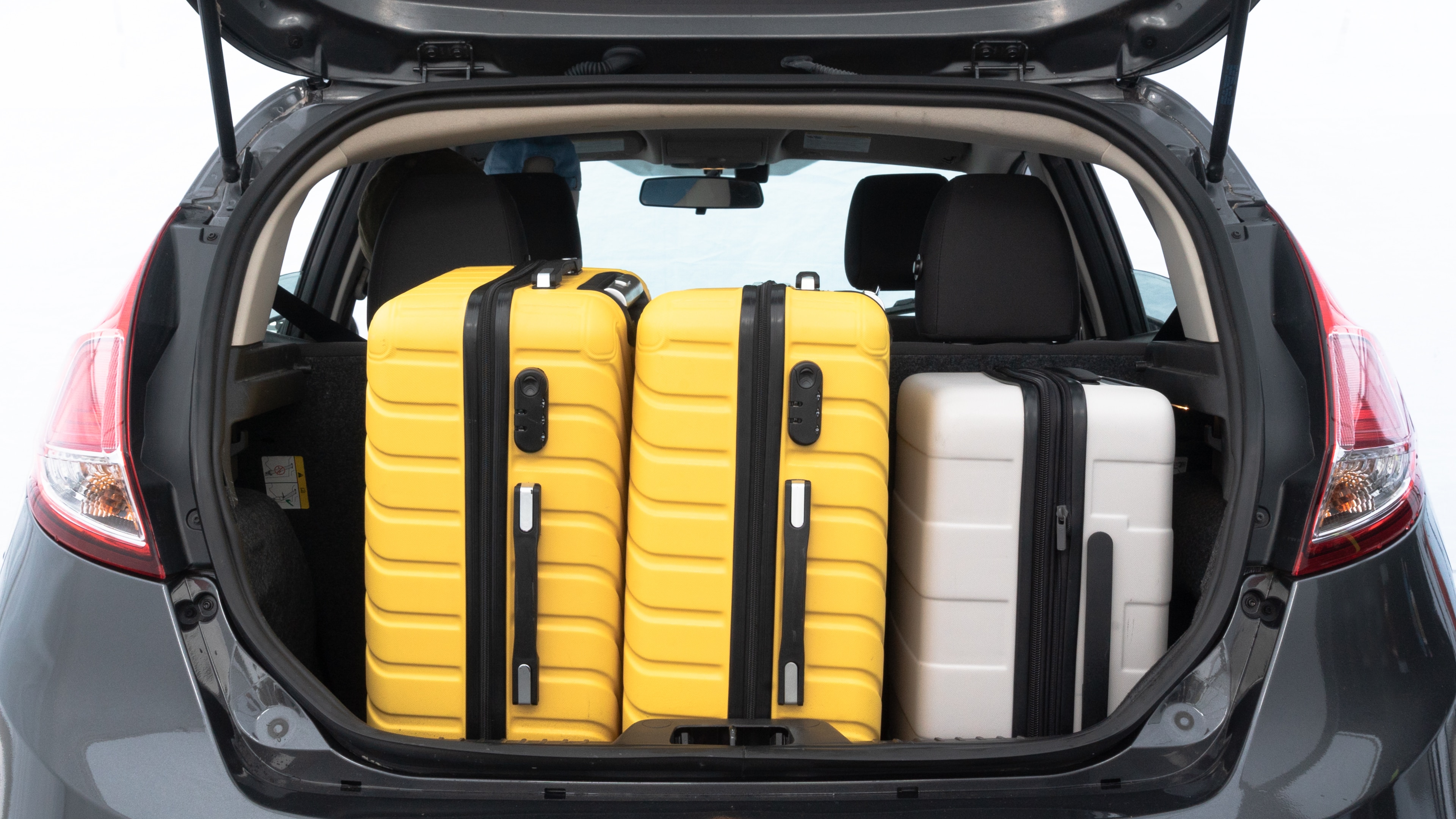 The trunk lid is open, showing full view of the trunk space. Two medium and one small suitcases are placed inside.