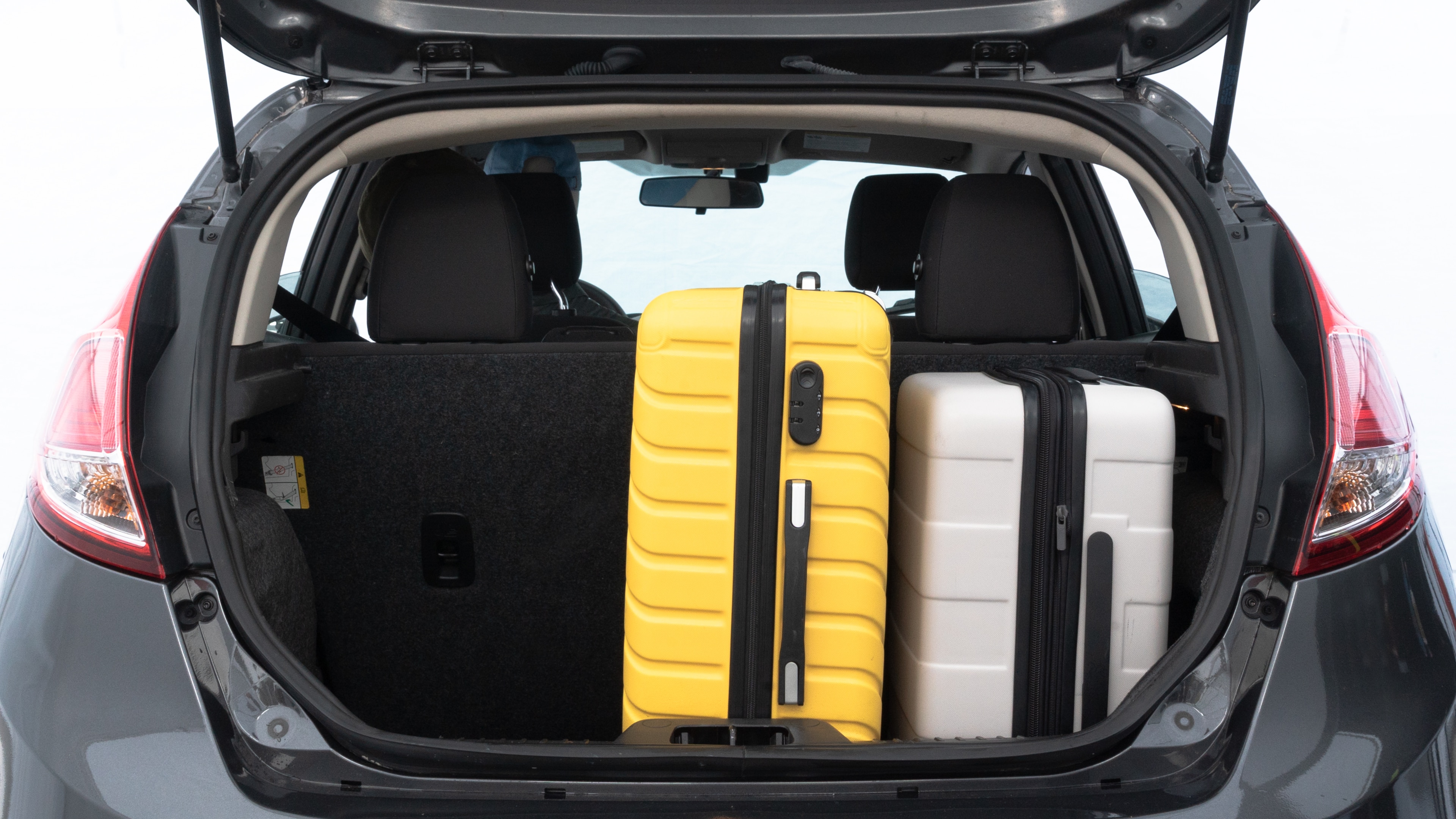 The trunk lid is open, showing full view of the trunk space. Two medium and one small suitcases are placed inside.