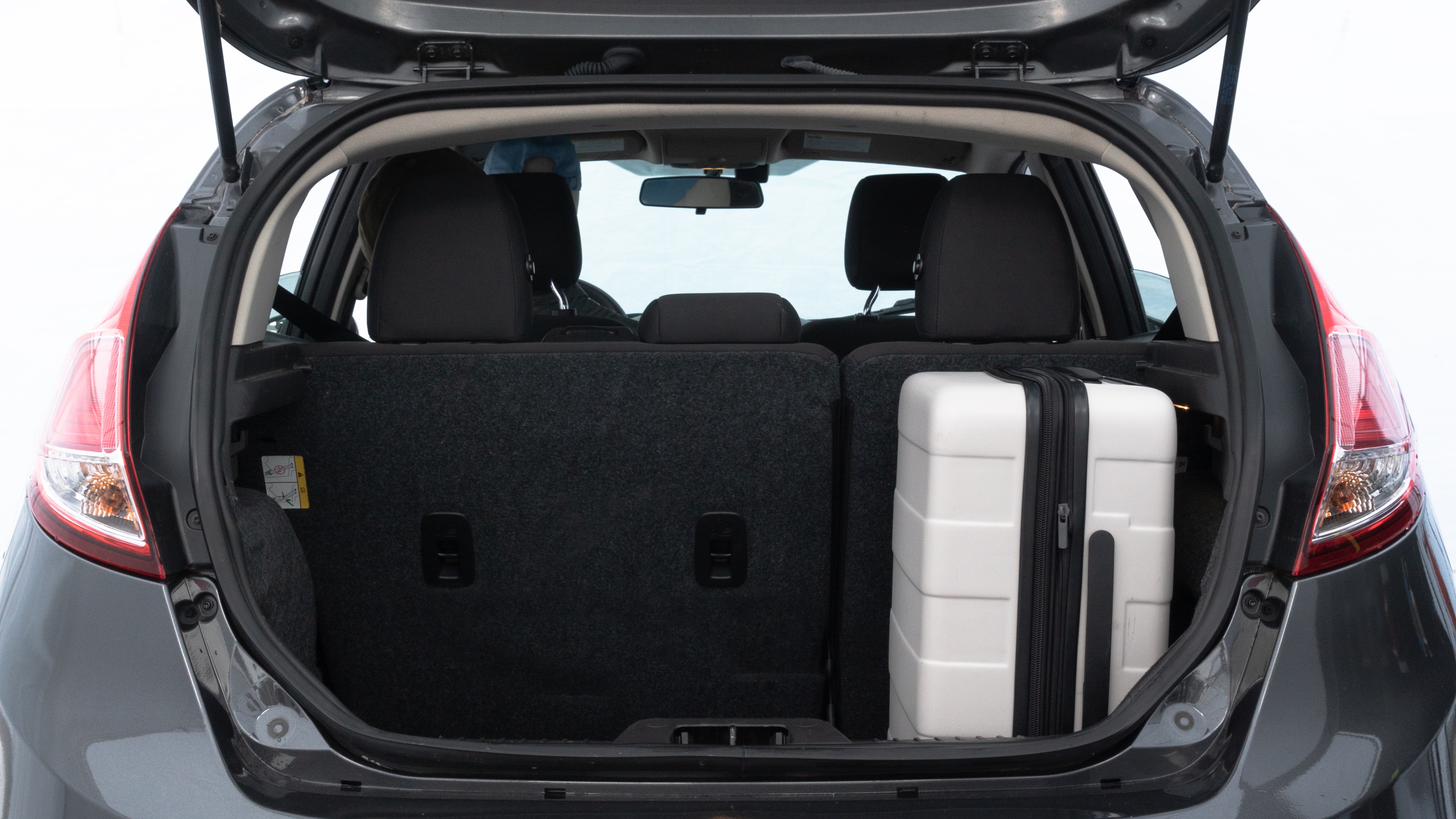 The trunk lid is open, showing full view of the trunk space. Two medium and one small suitcases are placed inside.