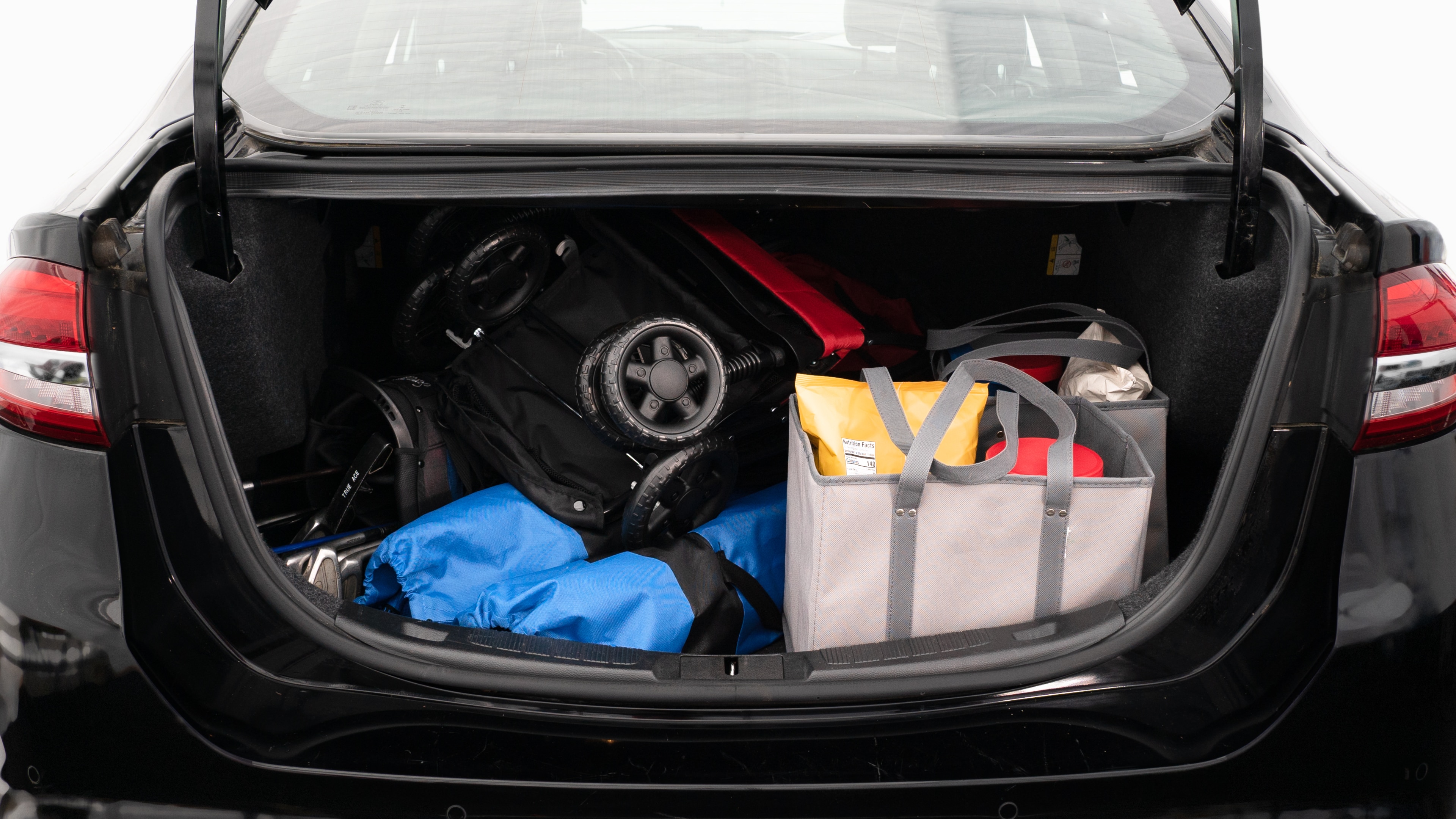 The trunk lid is open showing full view of the trunk. A baby stroller, two grocery carriers, two camping chairs in the carrying bag, and a set of golf clubs are placed inside.