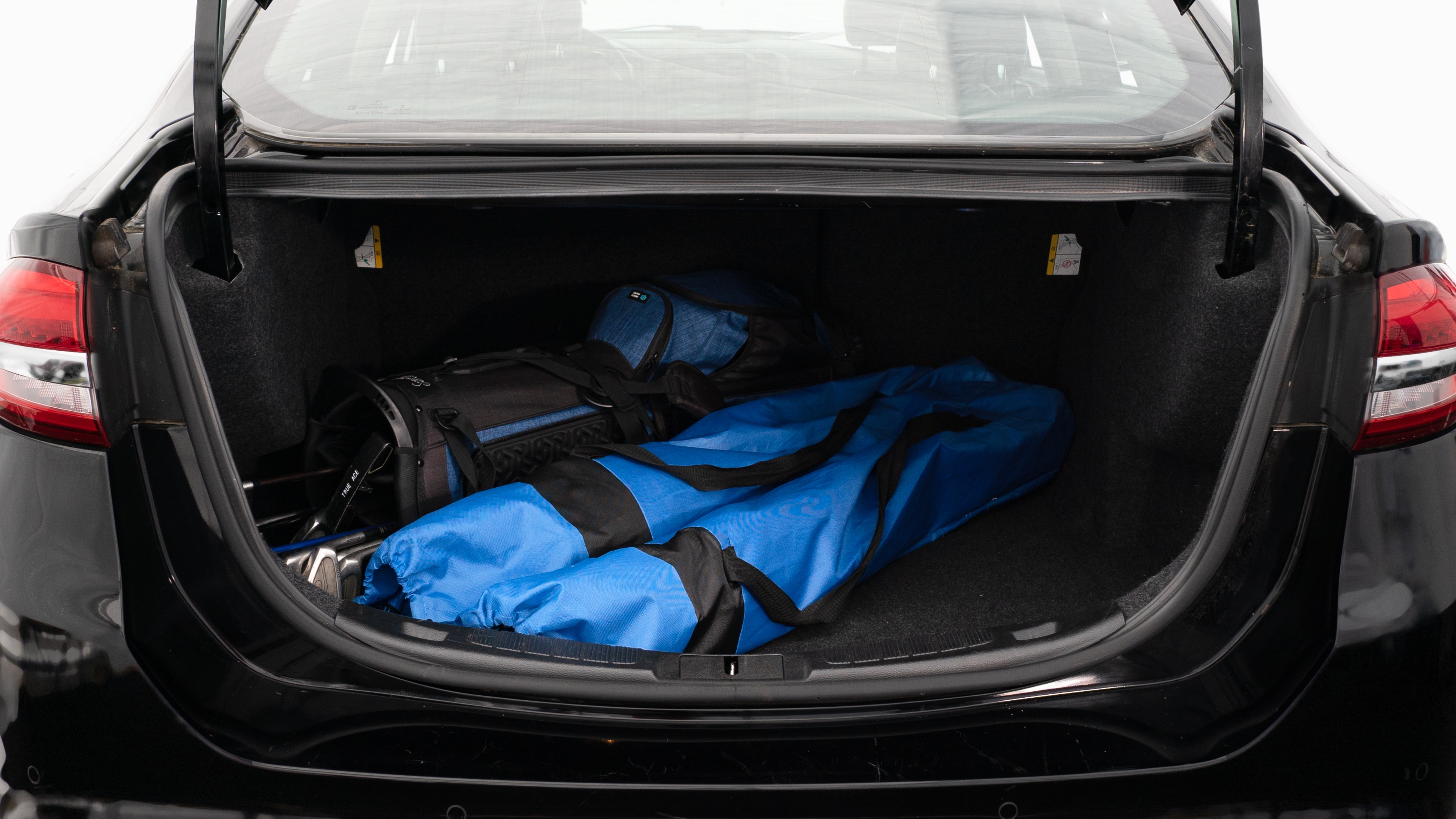 The trunk lid is open showing full view of the trunk. A baby stroller, two grocery carriers, two camping chairs in the carrying bag, and a set of golf clubs are placed inside.