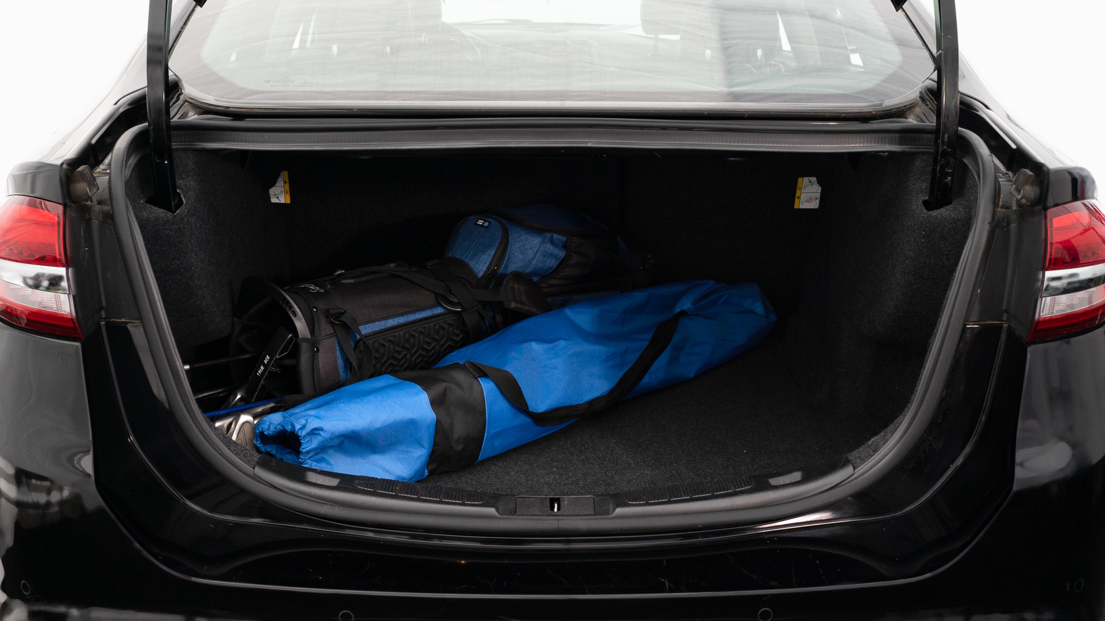 The trunk lid is open showing full view of the trunk. A baby stroller, two grocery carriers, two camping chairs in the carrying bag, and a set of golf clubs are placed inside.