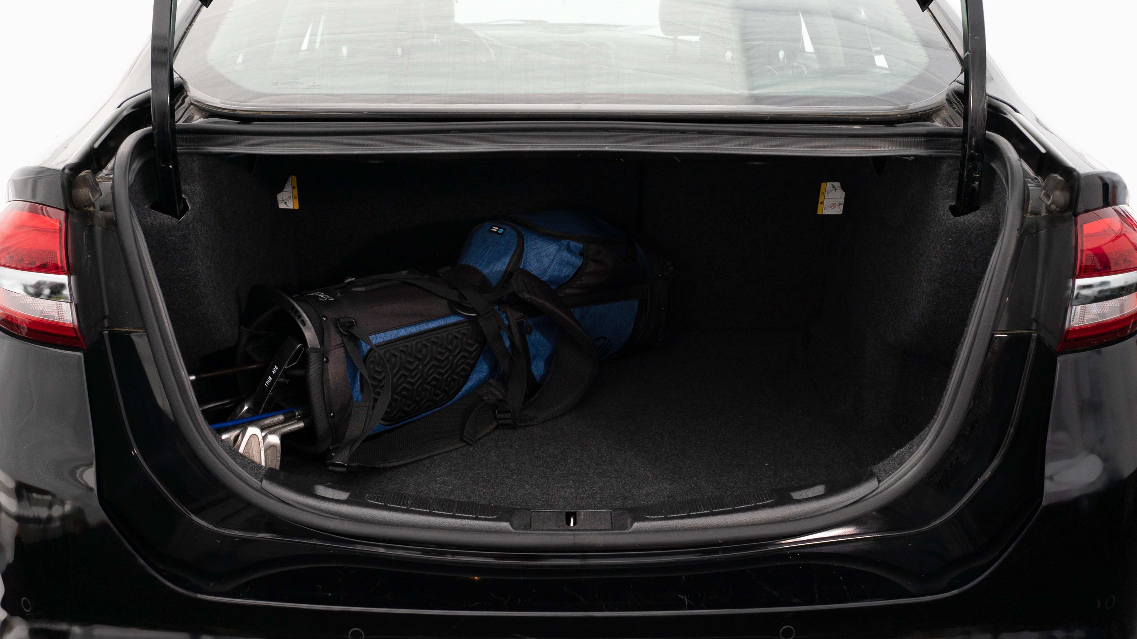 The trunk lid is open showing full view of the trunk. A baby stroller, two grocery carriers, two camping chairs in the carrying bag, and a set of golf clubs are placed inside.
