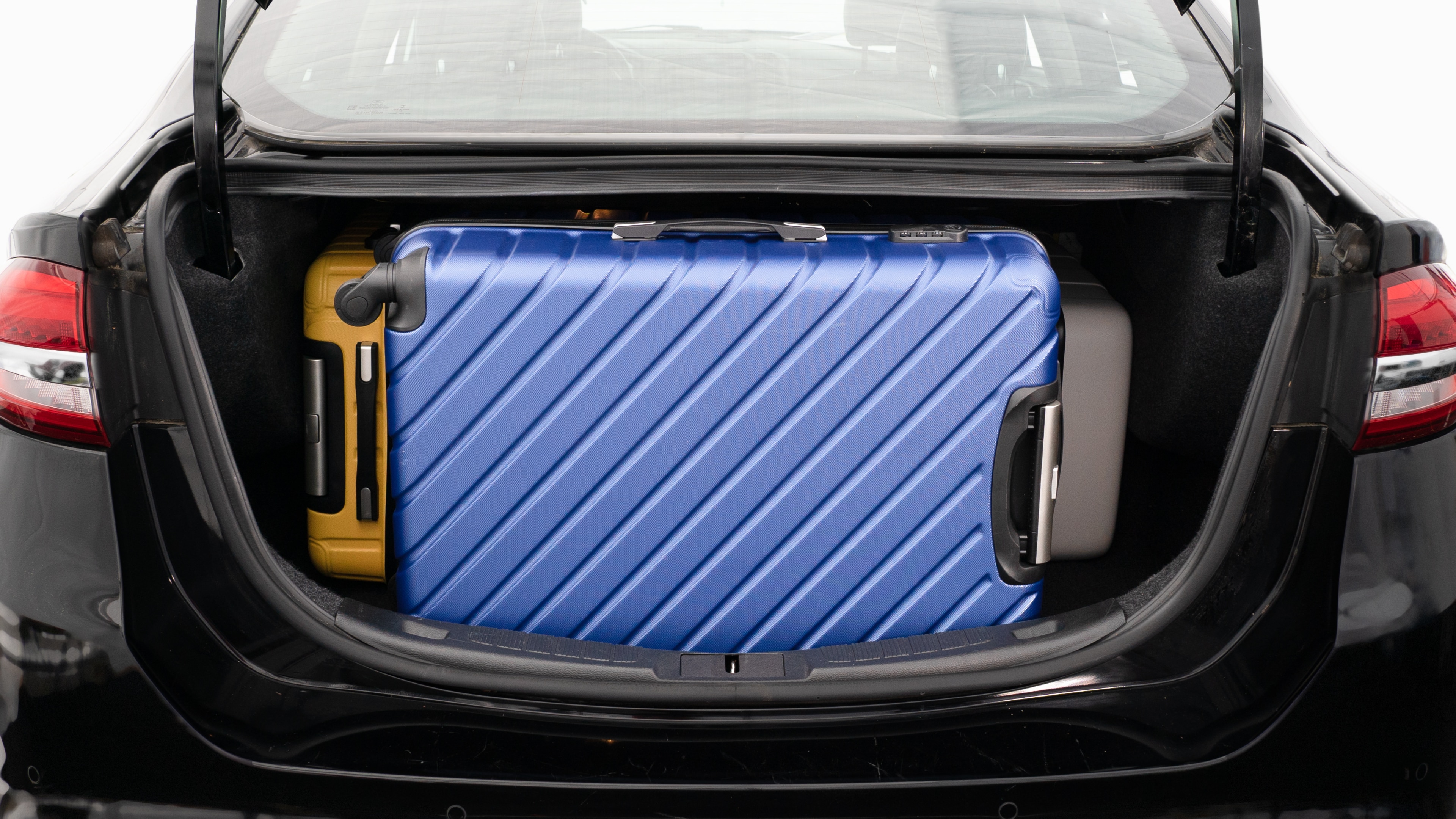The trunk lid is open, showing a full view of the trunk space. Three large and two small suitcases are place inside