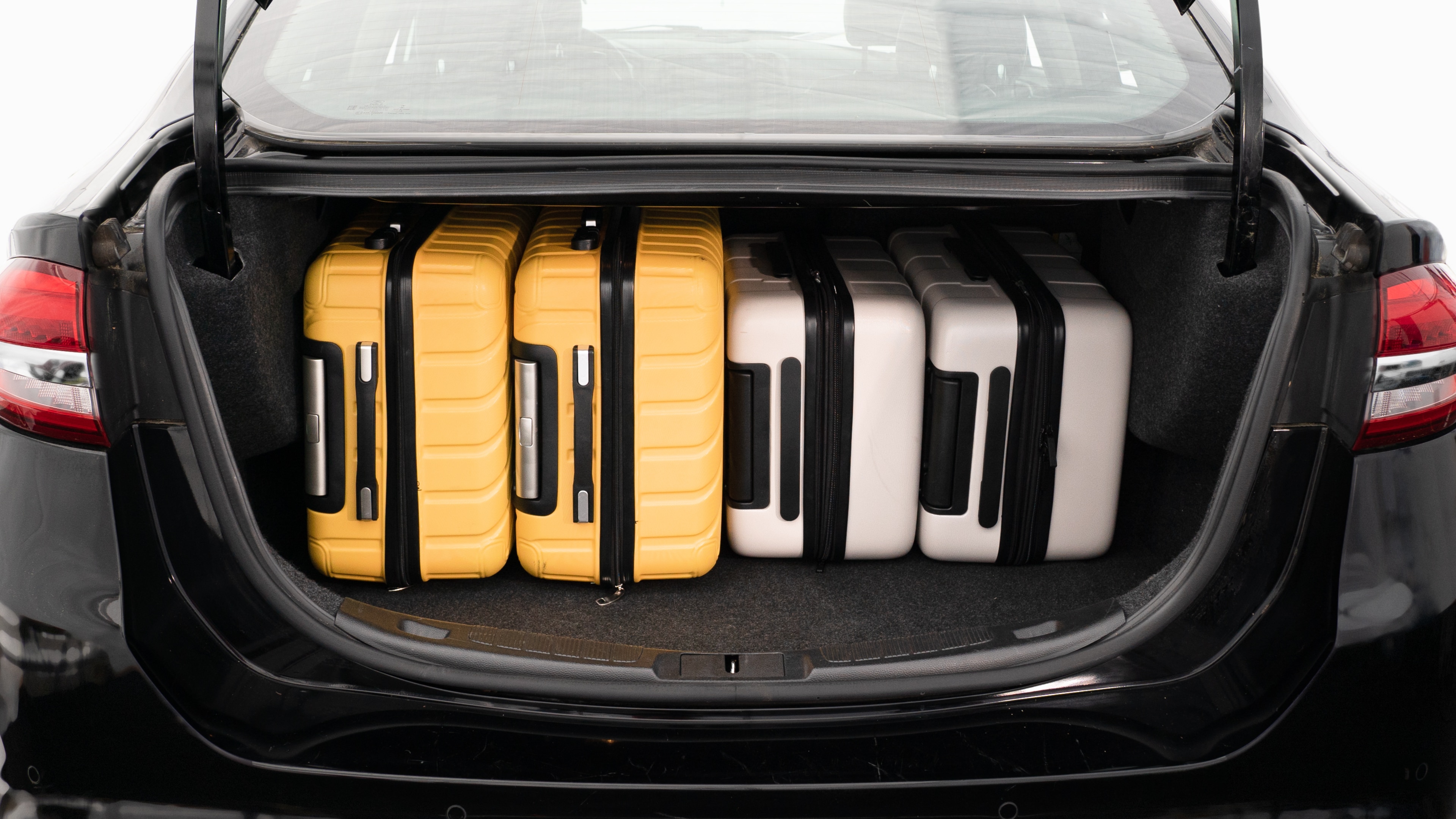 The trunk lid is open, showing a full view of the trunk space. Three large and two small suitcases are place inside