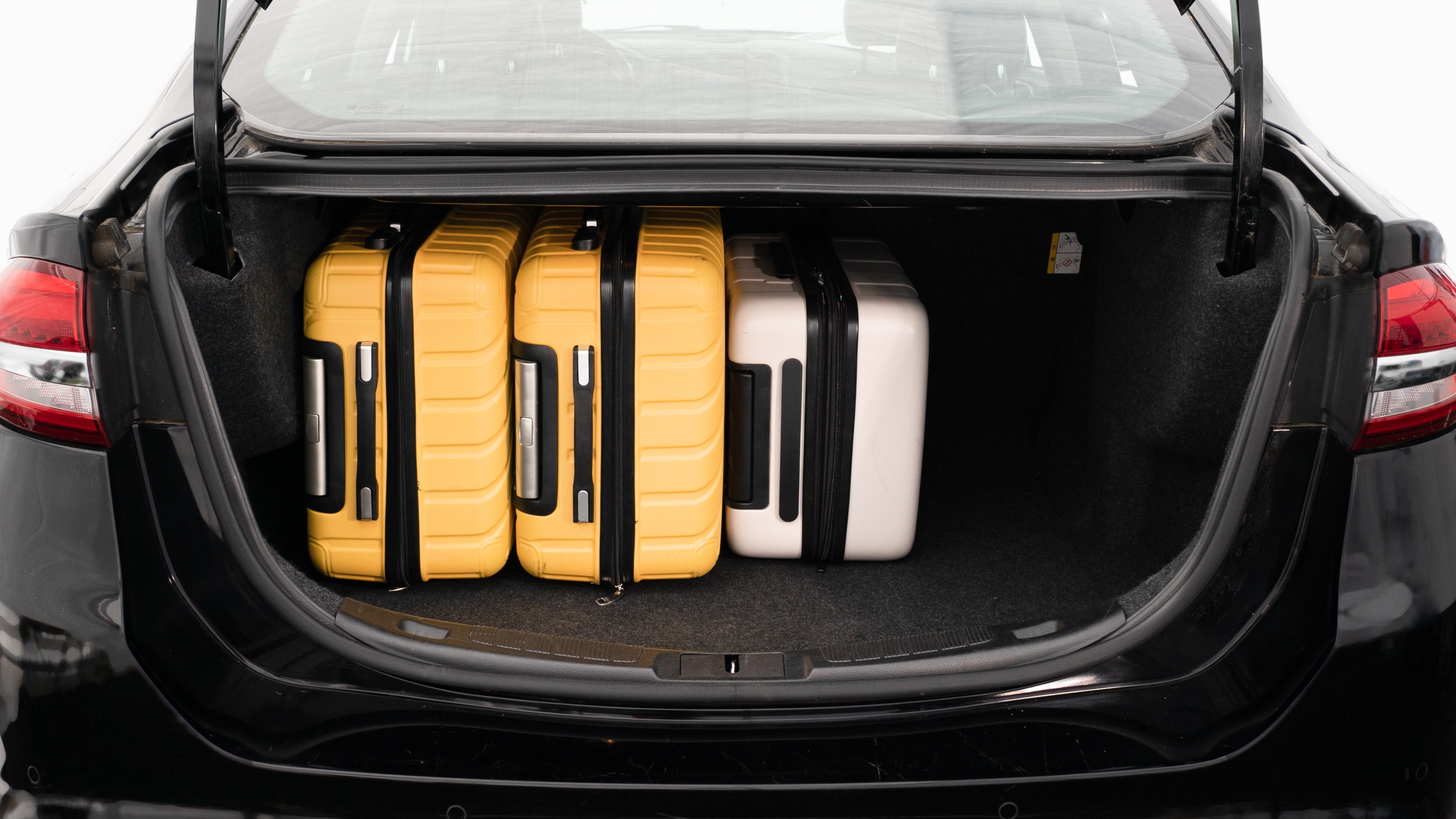 The trunk lid is open, showing a full view of the trunk space. Three large and two small suitcases are place inside