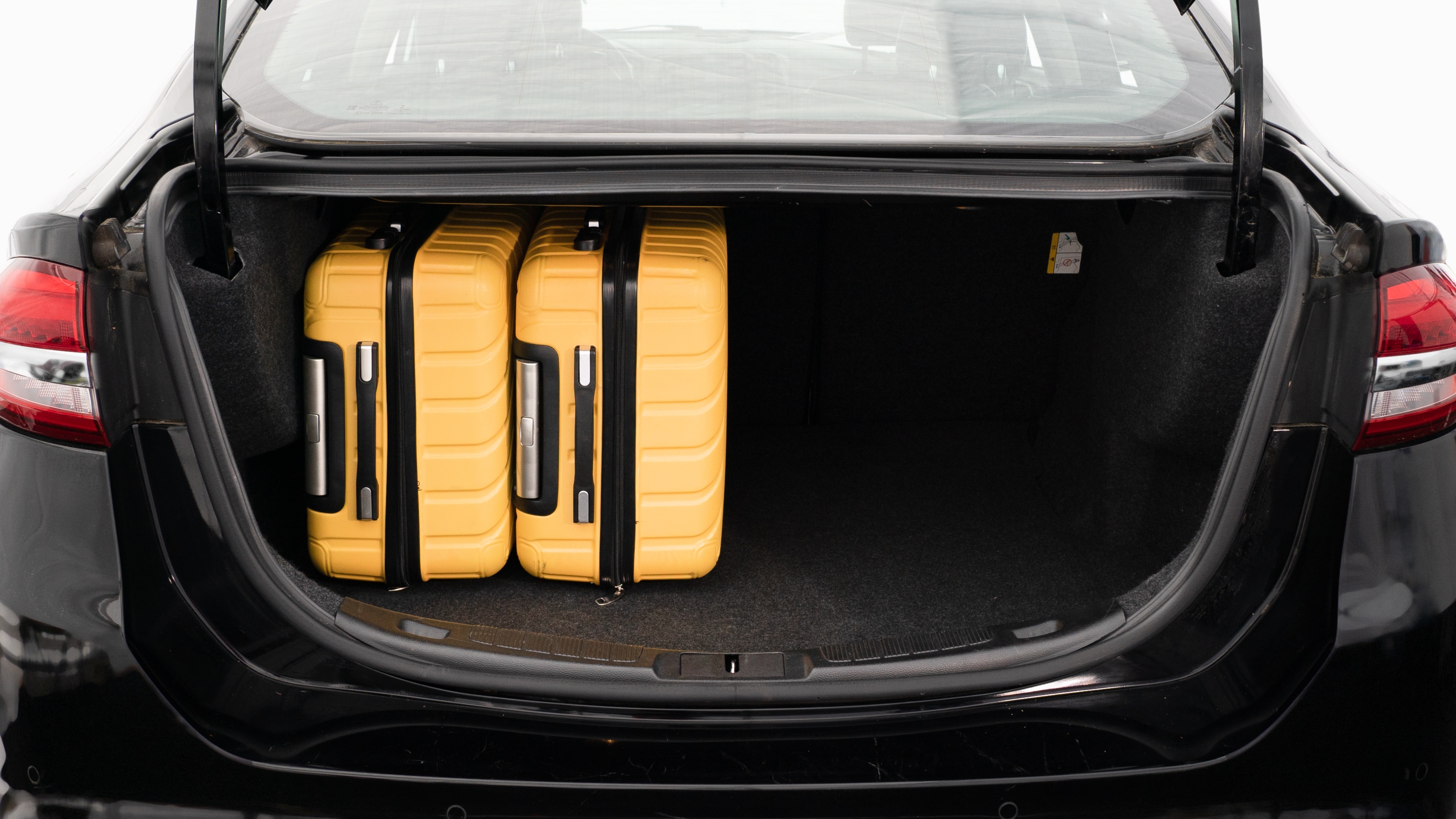 The trunk lid is open, showing a full view of the trunk space. Three large and two small suitcases are place inside