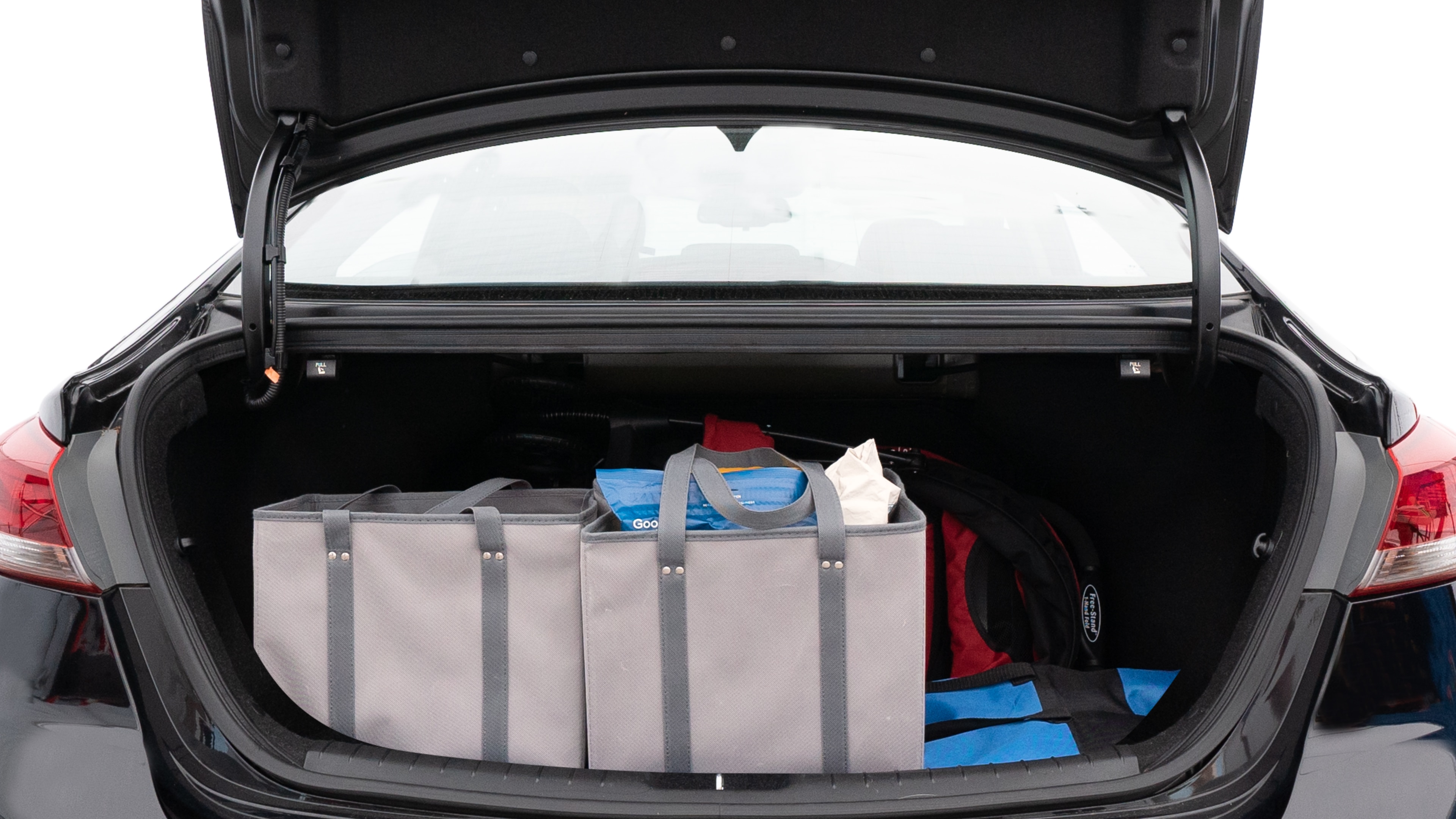 The trunk lid is open showing full view of the trunk. A baby stroller, three grocery carriers, two camping chairs in the carrying bag, and a set of golf clubs are placed inside.