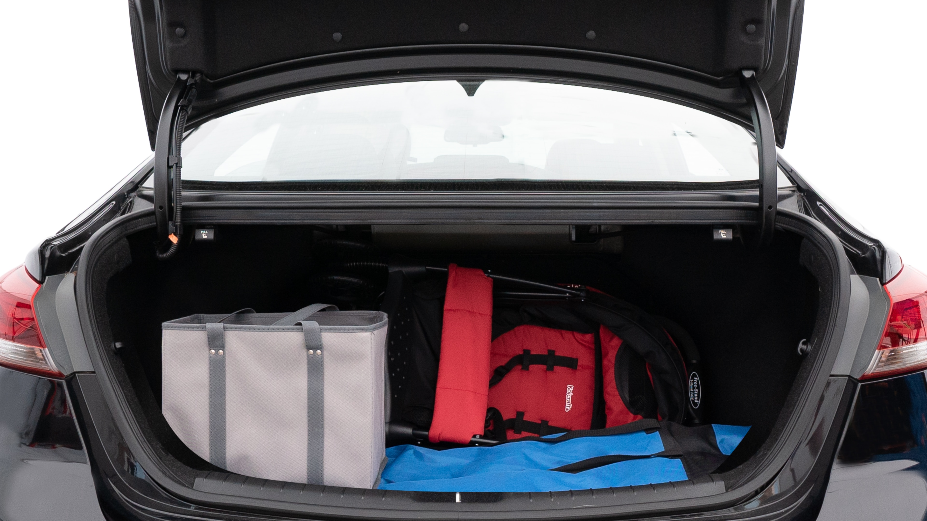 The trunk lid is open showing full view of the trunk. A baby stroller, three grocery carriers, two camping chairs in the carrying bag, and a set of golf clubs are placed inside.