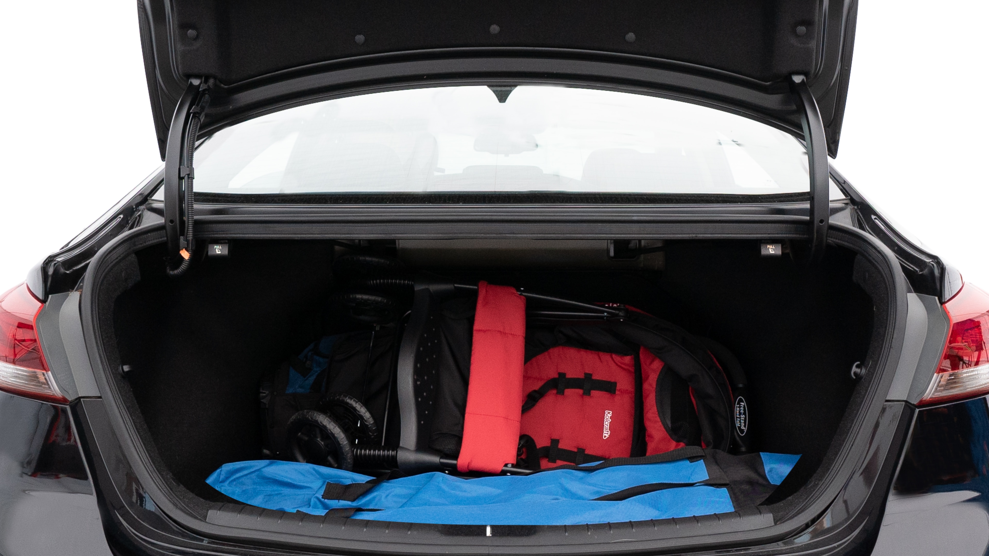 The trunk lid is open showing full view of the trunk. A baby stroller, three grocery carriers, two camping chairs in the carrying bag, and a set of golf clubs are placed inside.