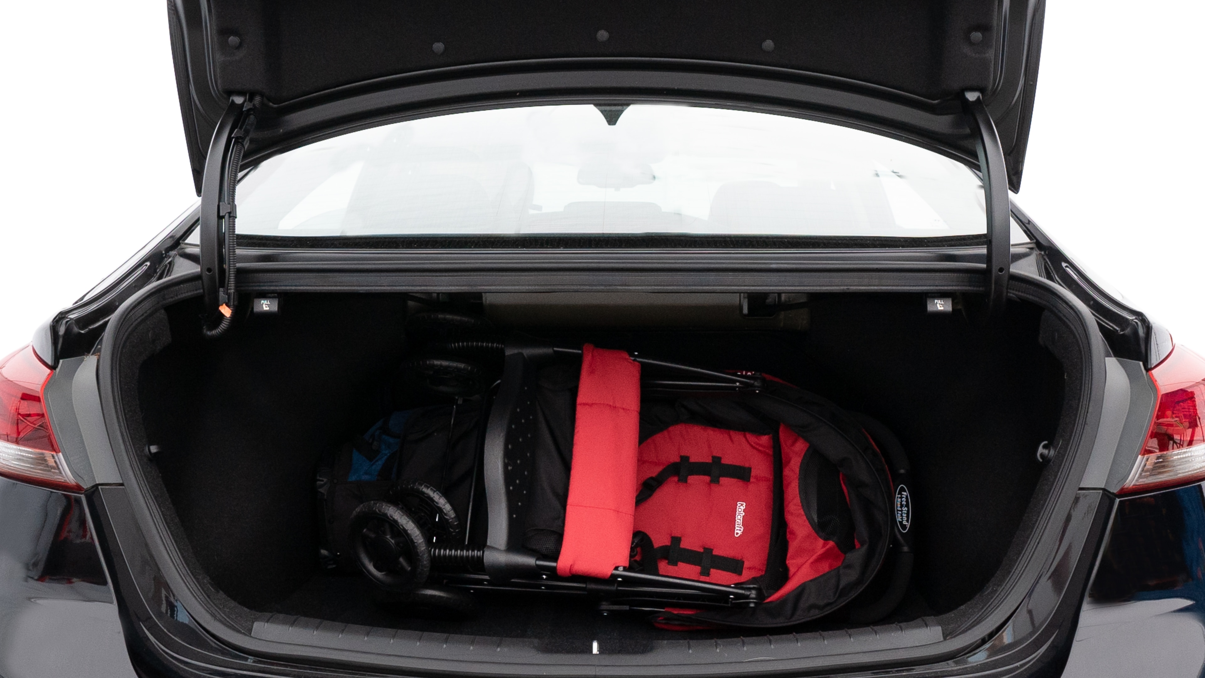 The trunk lid is open showing full view of the trunk. A baby stroller, three grocery carriers, two camping chairs in the carrying bag, and a set of golf clubs are placed inside.