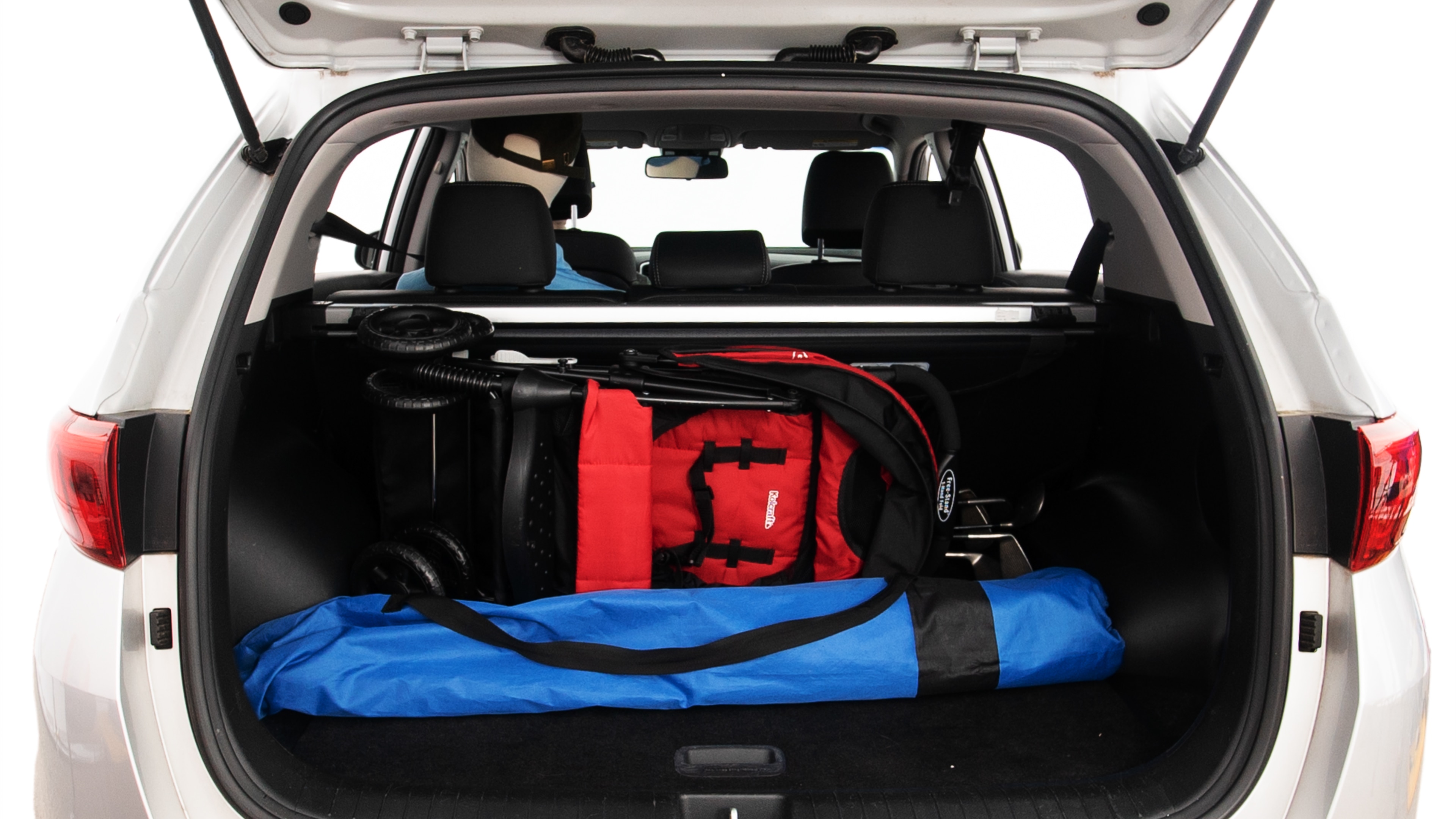 The trunk lid is open showing full view of the trunk. A baby stroller, three grocery carriers, two camping chairs in the carrying bag, and a set of golf clubs are placed inside.