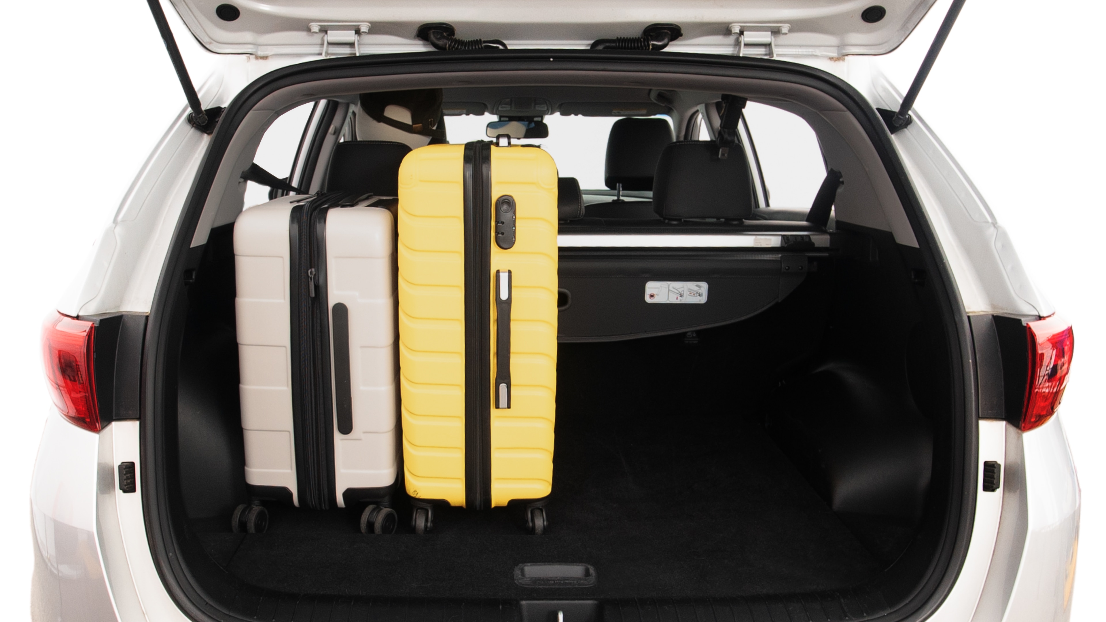 The trunk lid is open, showing full view of the trunk space. Two large and two small suitcases are placed inside.