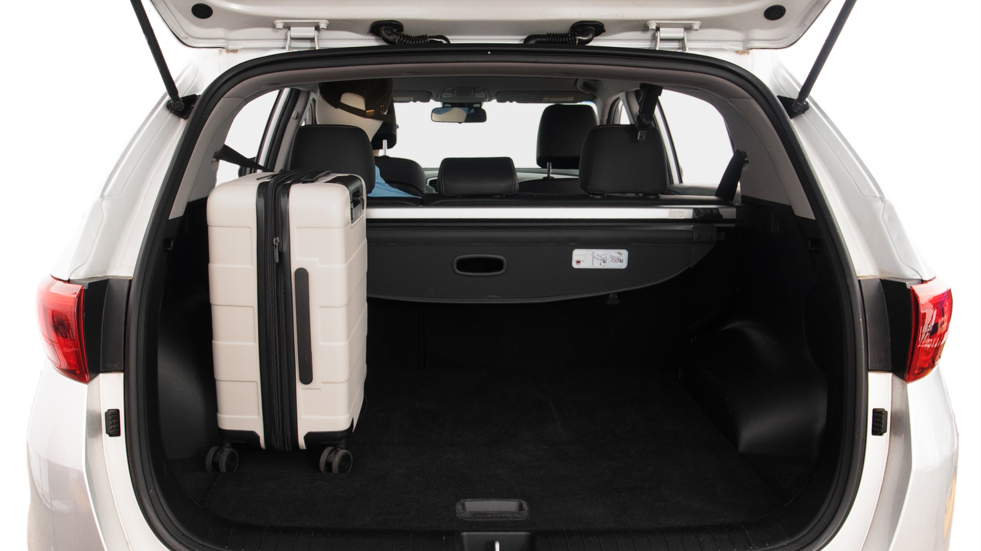 The trunk lid is open, showing full view of the trunk space. Two large and two small suitcases are placed inside.