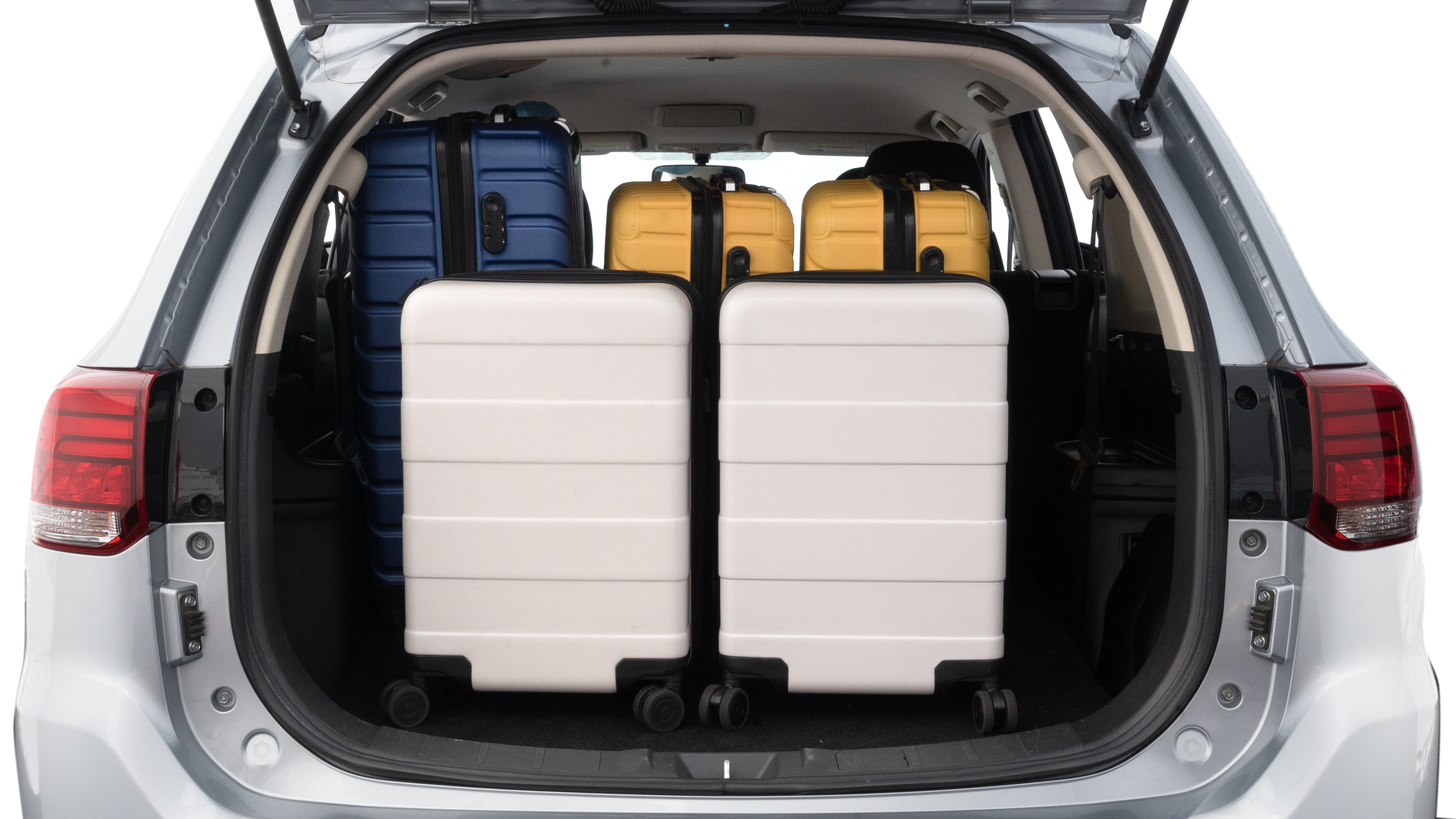 The trunk lid is open, showing full view of the trunk space. One large, two medium, and two small suitcases are placed inside.