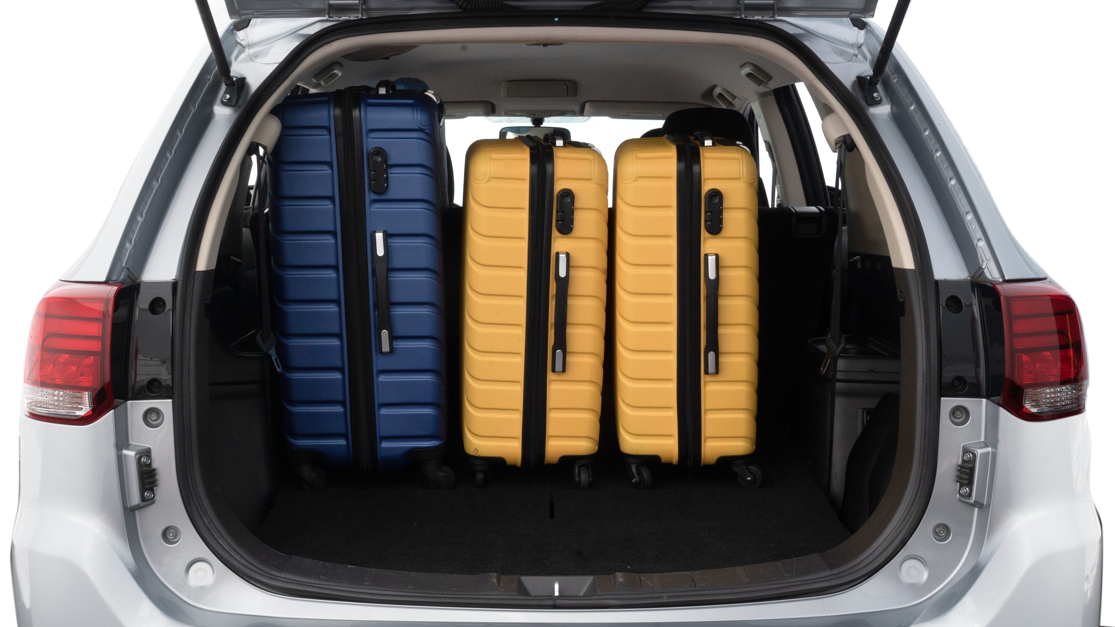 The trunk lid is open, showing full view of the trunk space. One large, two medium, and two small suitcases are placed inside.