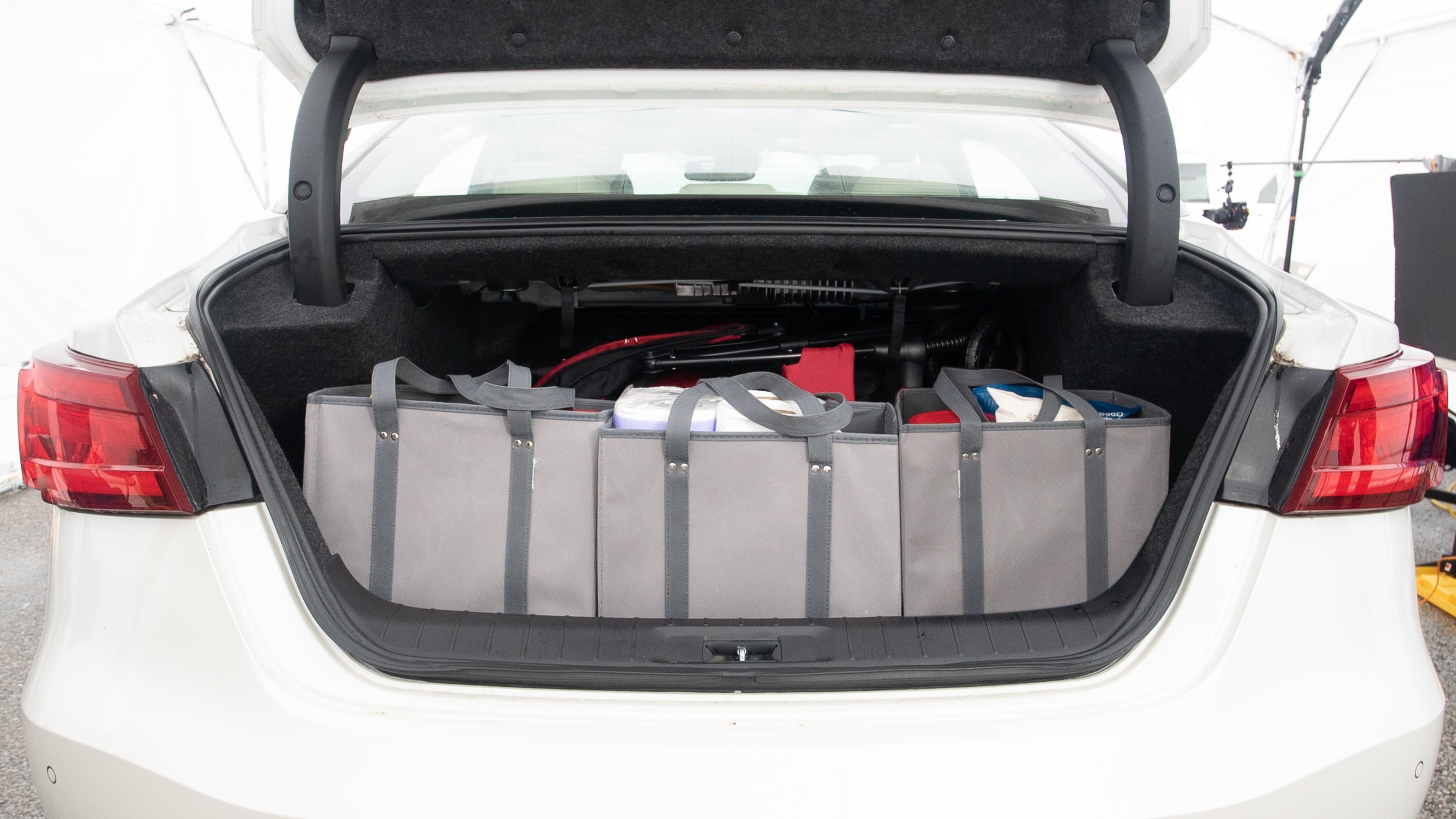 The trunk lid is open showing full view of the trunk. A baby stroller, three grocery carriers, one camping chairs in the carrying bag, and a set of golf clubs are placed inside.