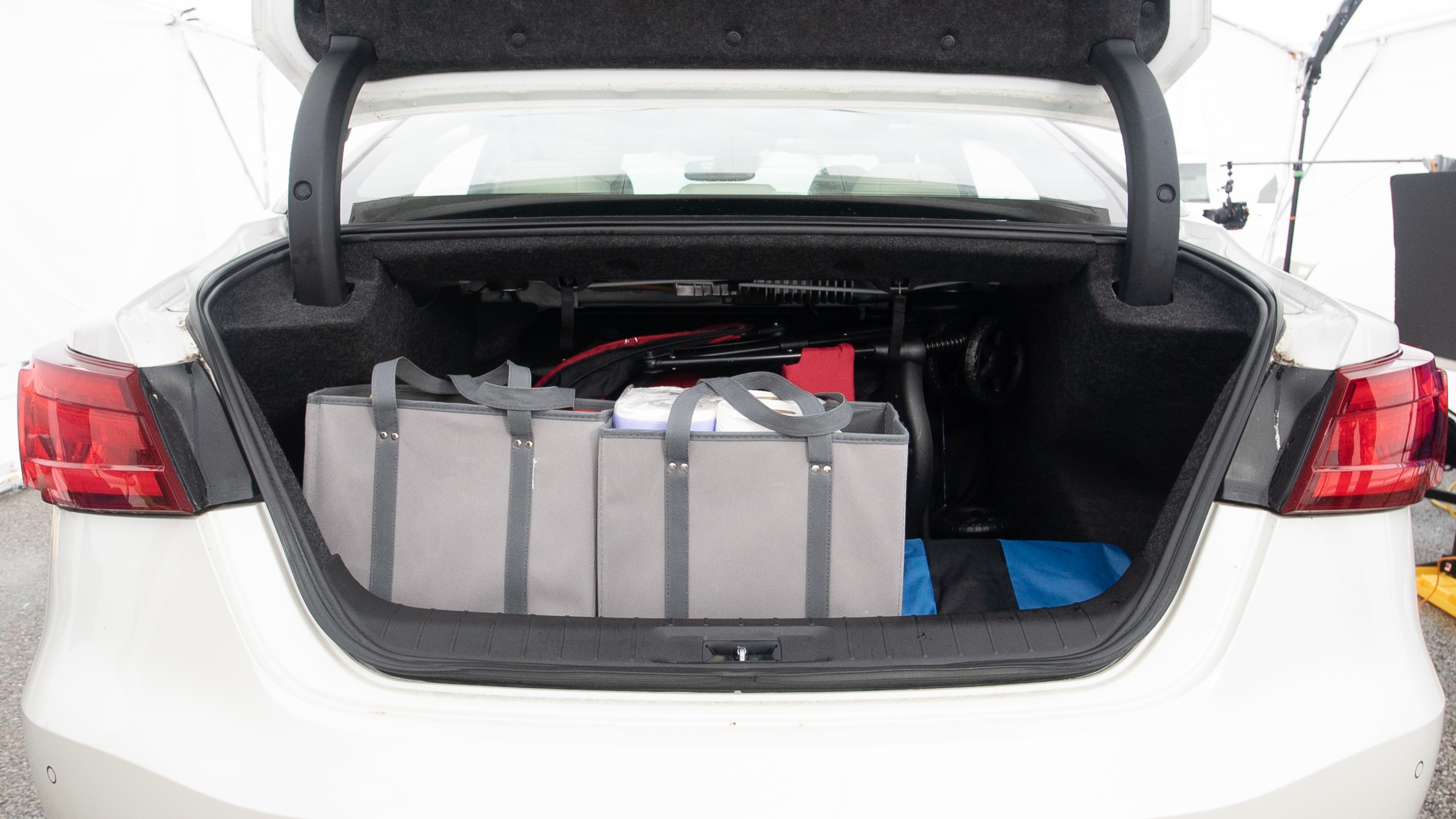 The trunk lid is open showing full view of the trunk. A baby stroller, three grocery carriers, one camping chairs in the carrying bag, and a set of golf clubs are placed inside.